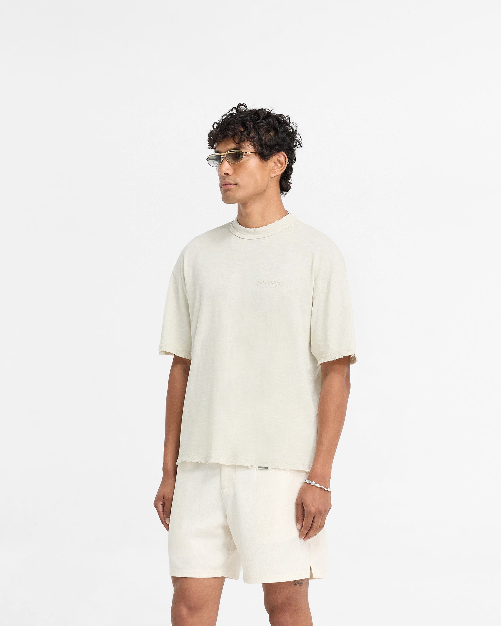 Back product image of a mens white t-shirt on a plain white background | Slub T-Shirt in White Sand | T-Shirt with tonal embroidered branding and raw hems | FW24 T-Shirts | Represent Clo