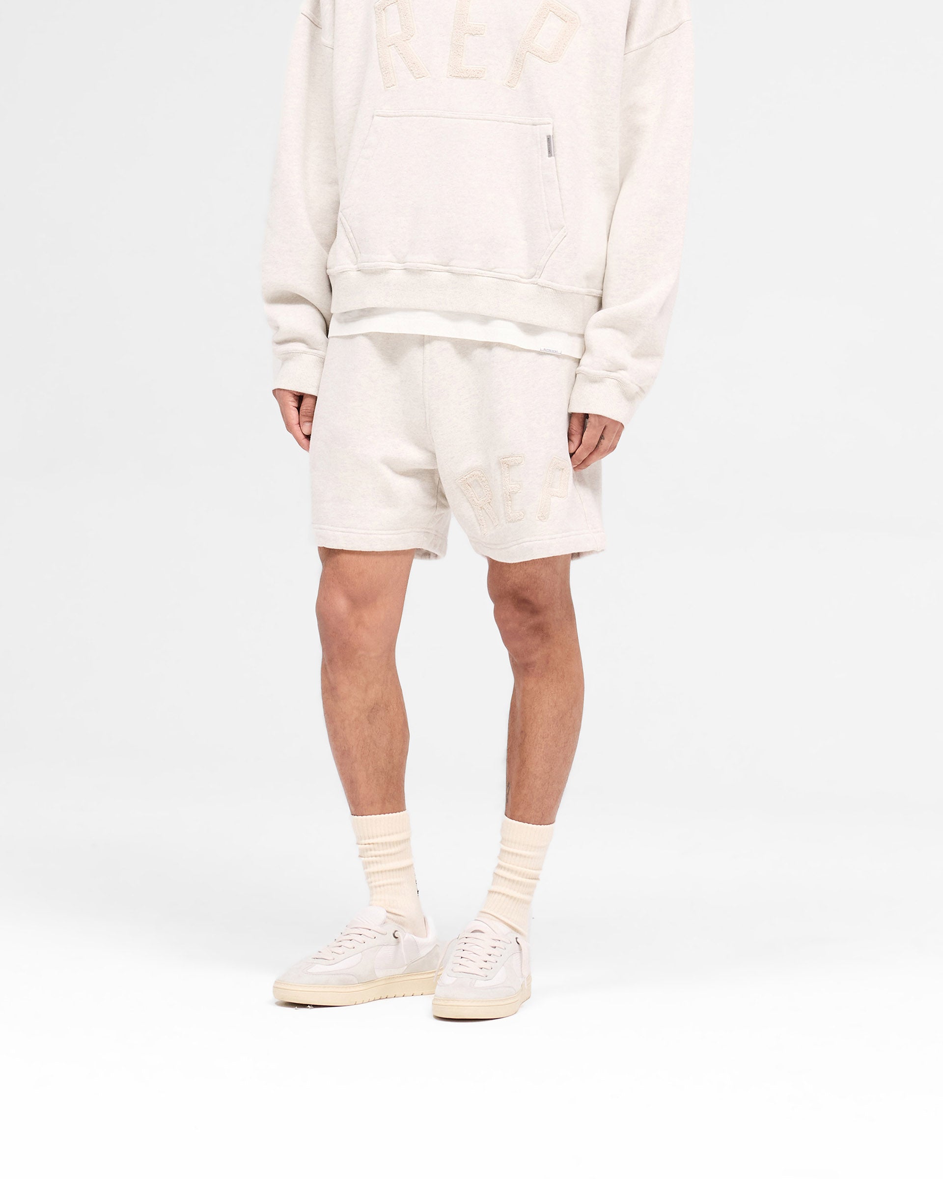 Back product image of mens cream shorts on a plain white background | Rep Applique Shorts in Cream Marl | Shorts with elasticated waistband and applique logo | SS25 Shorts | Represent Clo