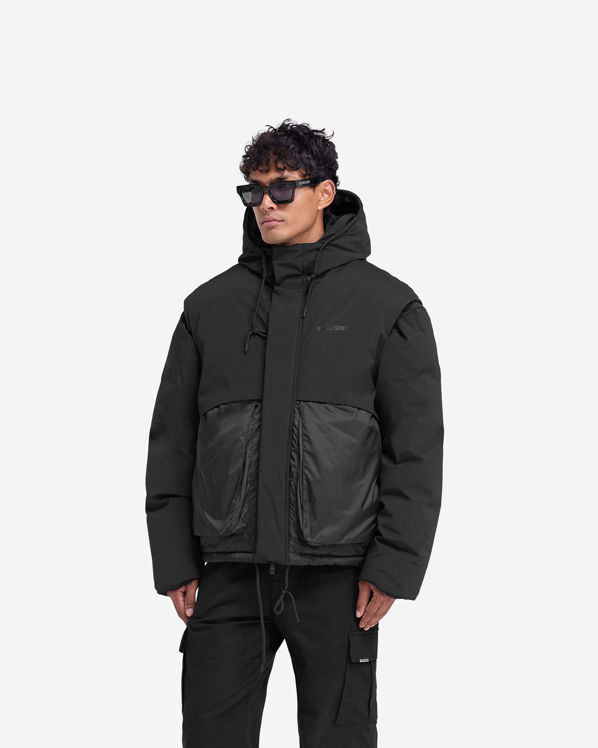 Back product image of a mens black puffer jacket on a plain white background | Layered Hooded Puffer in Jet Black | Duck down filled jacket with storm flaps | FW24 Outerwear | Represent Clo
