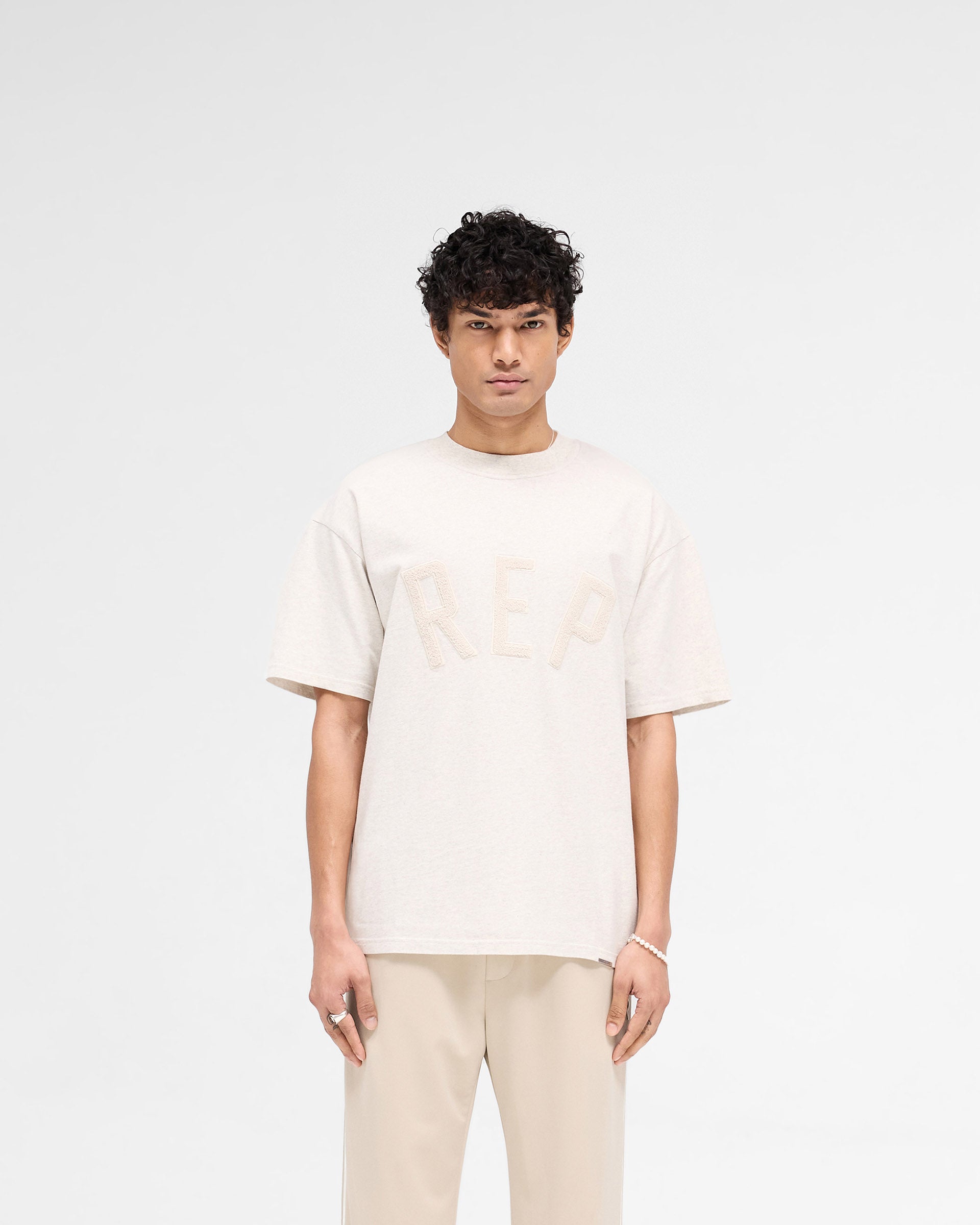 Back product image of a mens cream t-shirt on a plain white background | Rep Applique T-Shirt in Cream Marl | T-Shirt with overlock seams | SS25 T-Shirts | Represent Clo