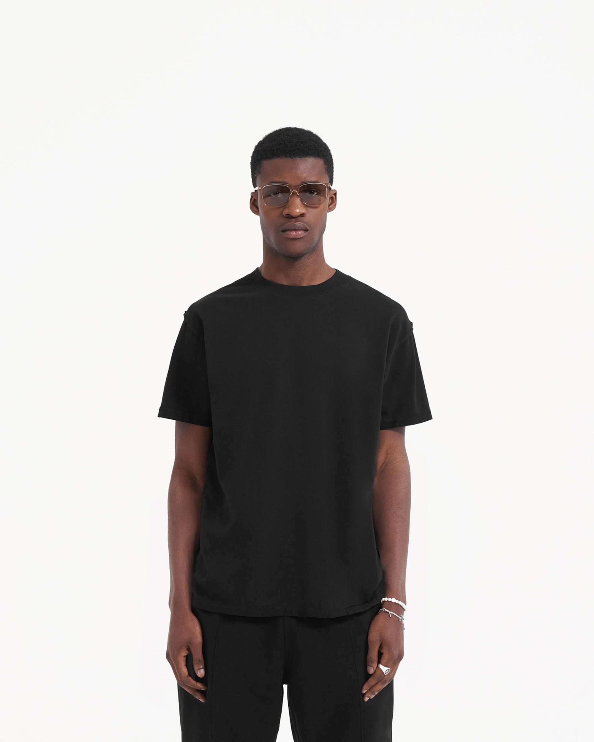 Man wearing a black t-shirt on a plain white background | Initial T-Shirt in Jet Black | Oversized t-shirt with external overlock seams | Initial T-Shirts | Represent Clo