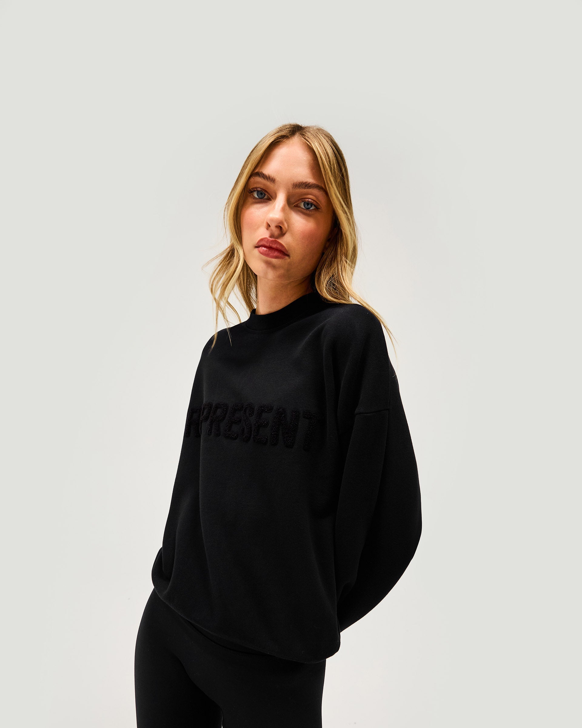 Woman wearing a black sweater on a plain white background | Owners Club Sweater in Jet Black | Relaxed fit sweater with embroidered branding | Womens Owners Club Sweaters | Represent Clo