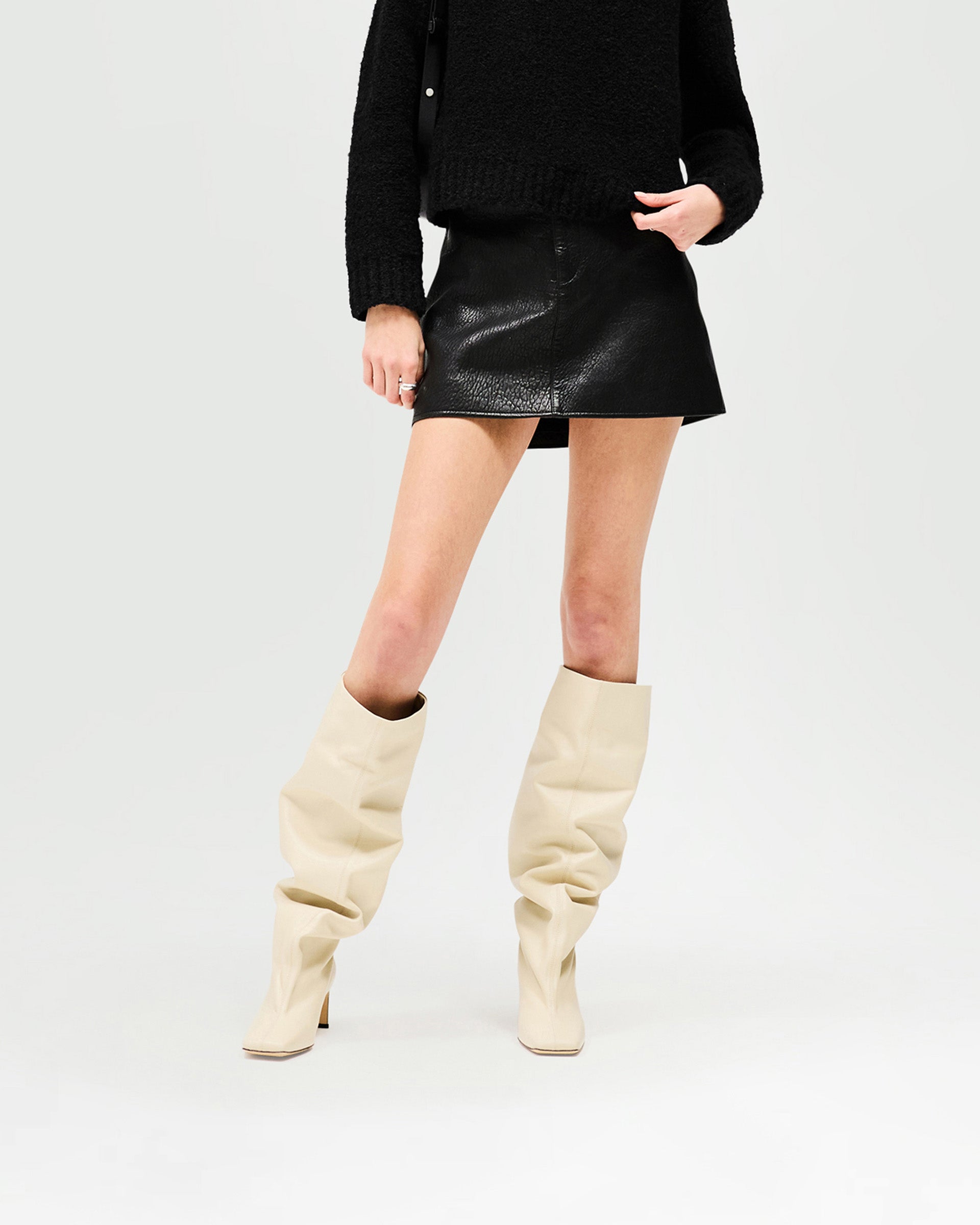 Woman wearing a black mini skirt on a plain white background | Drive Skirt in Jet Black | Bubble leather mini skirt with zip fly front | Womens SS25 Skirts | Represent Clo