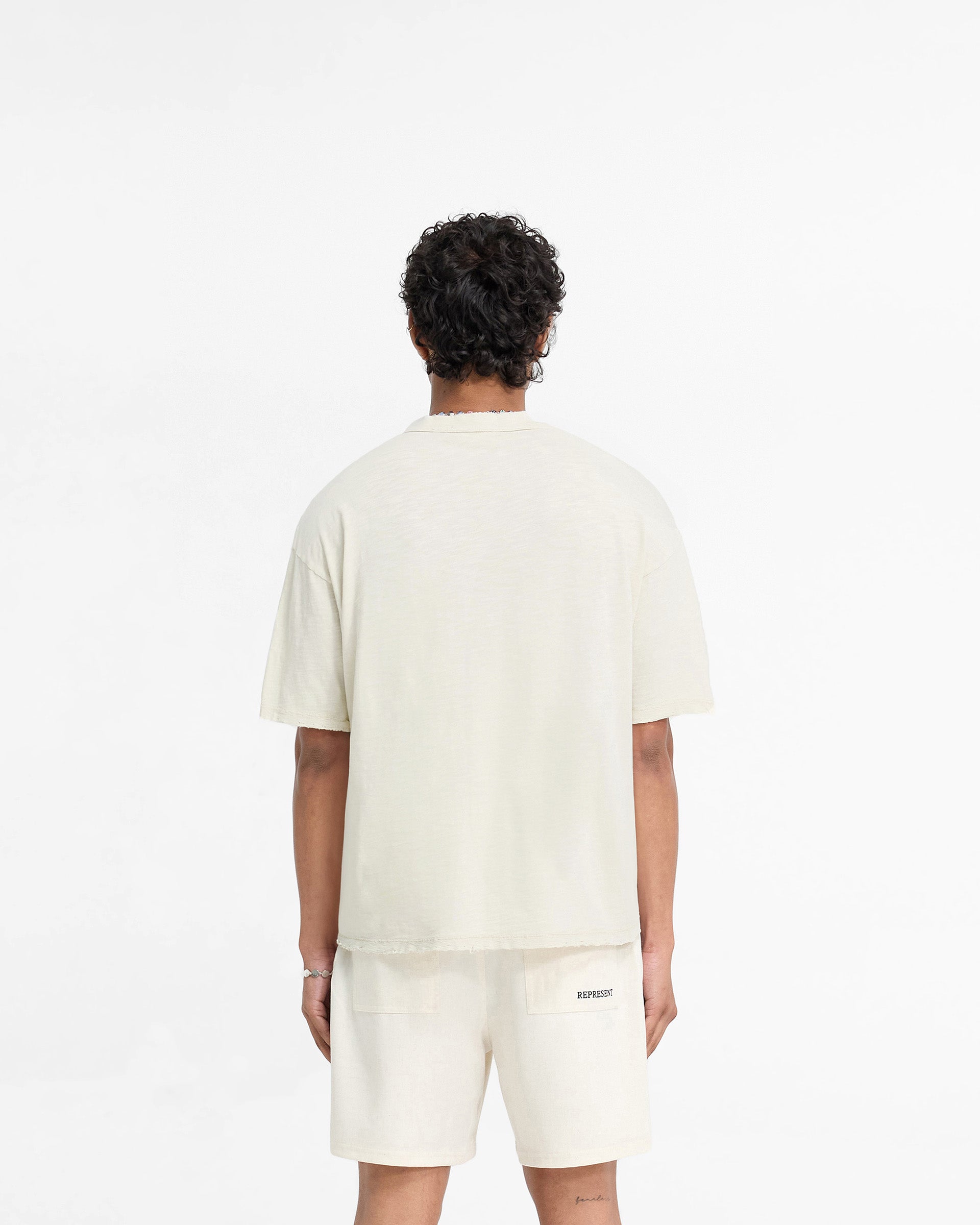 Man wearing a white t-shirt on a plain white background | Slub T-Shirt in White Sand | Oversized t-shirt with tonal embroidered branding | FW24 T-Shirts | Represent Clo