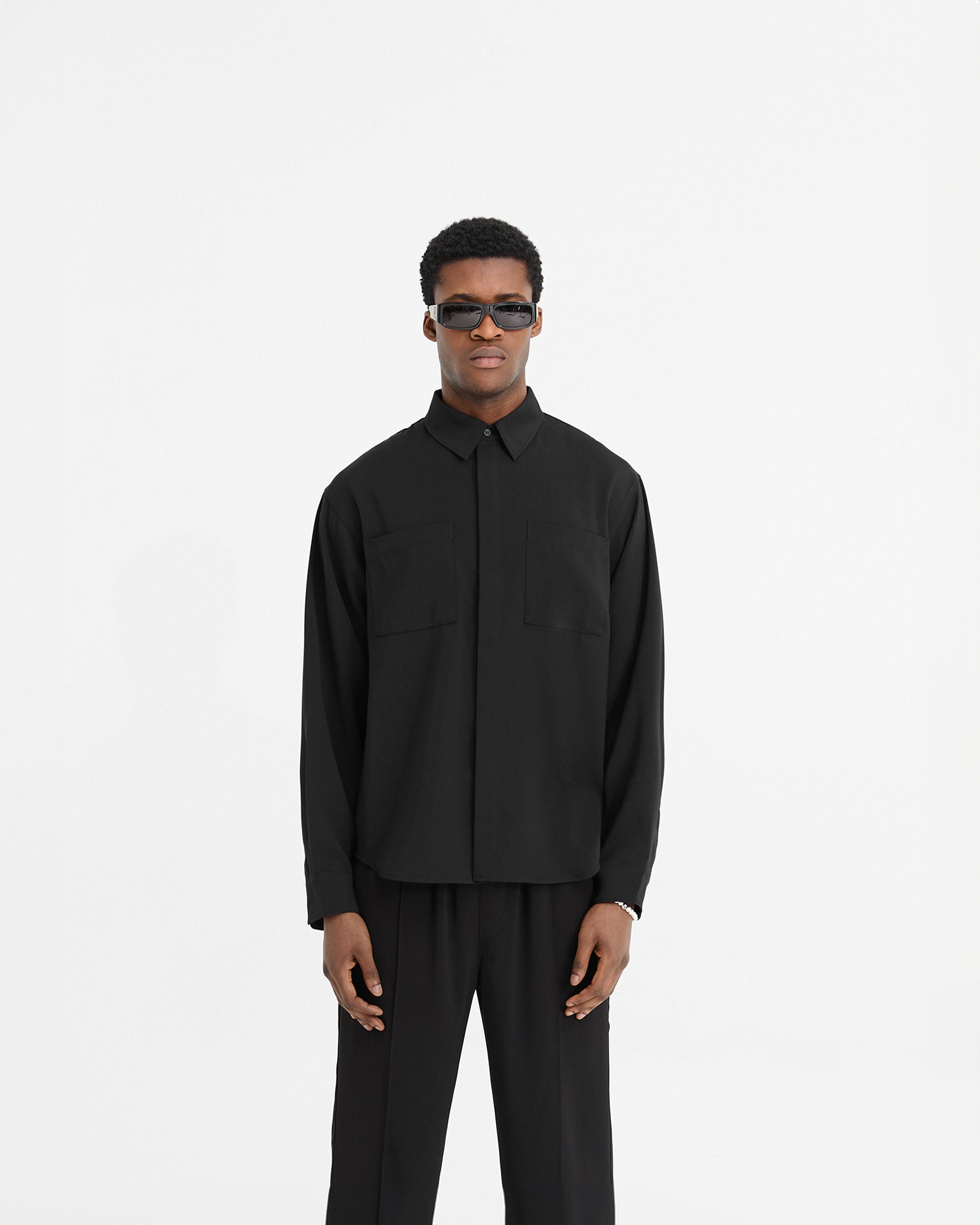 Man wearing a black shirt on a plain white background | Initial Shirt in Black | Slightly oversized black shirt with chest pockets and concealed placket | Initial Shirts | Represent Clo