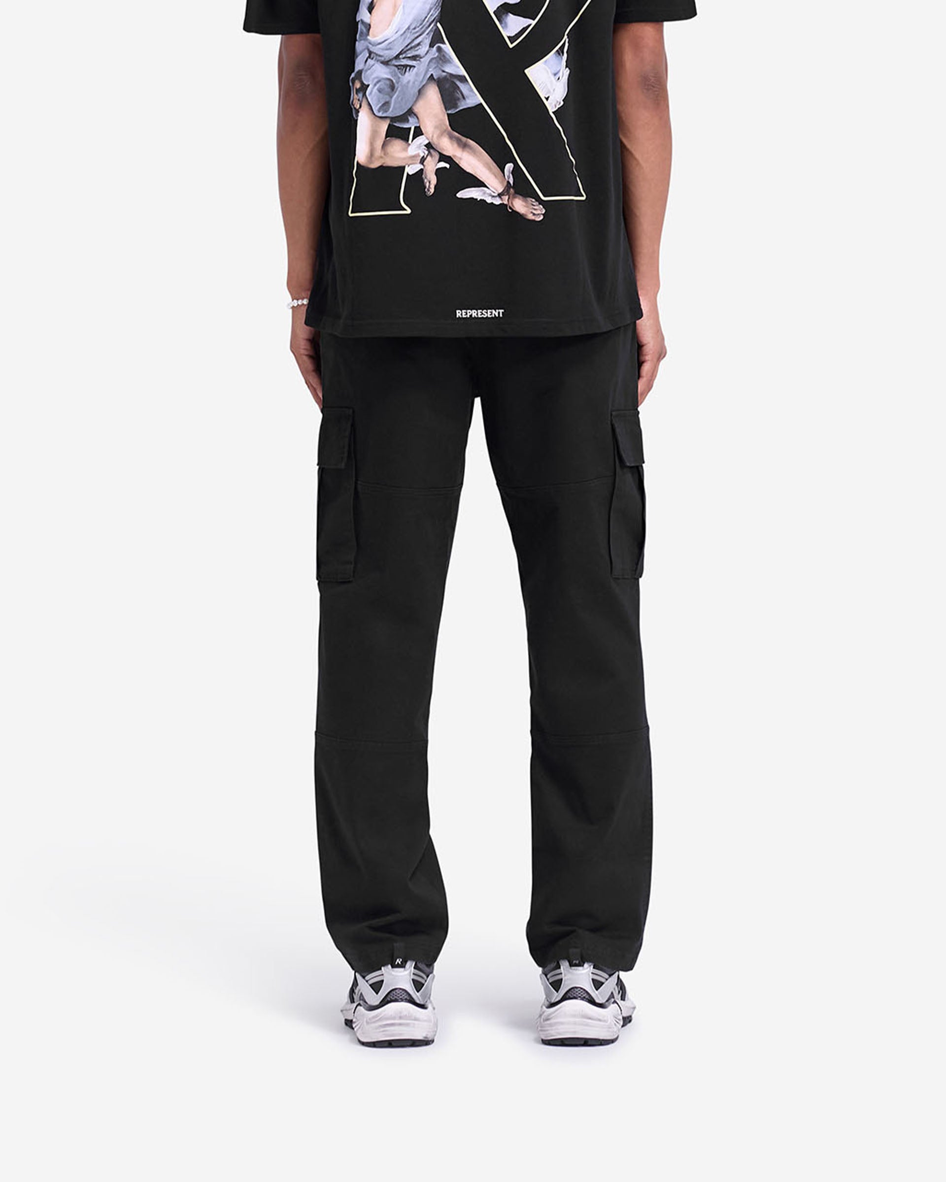 Man wearing black cargo pants on a plain white background | Cargo Pant in Black | Slim fit black cargo pants with elasticated waistband and flap pockets | FW24 Pants | Represent Clo