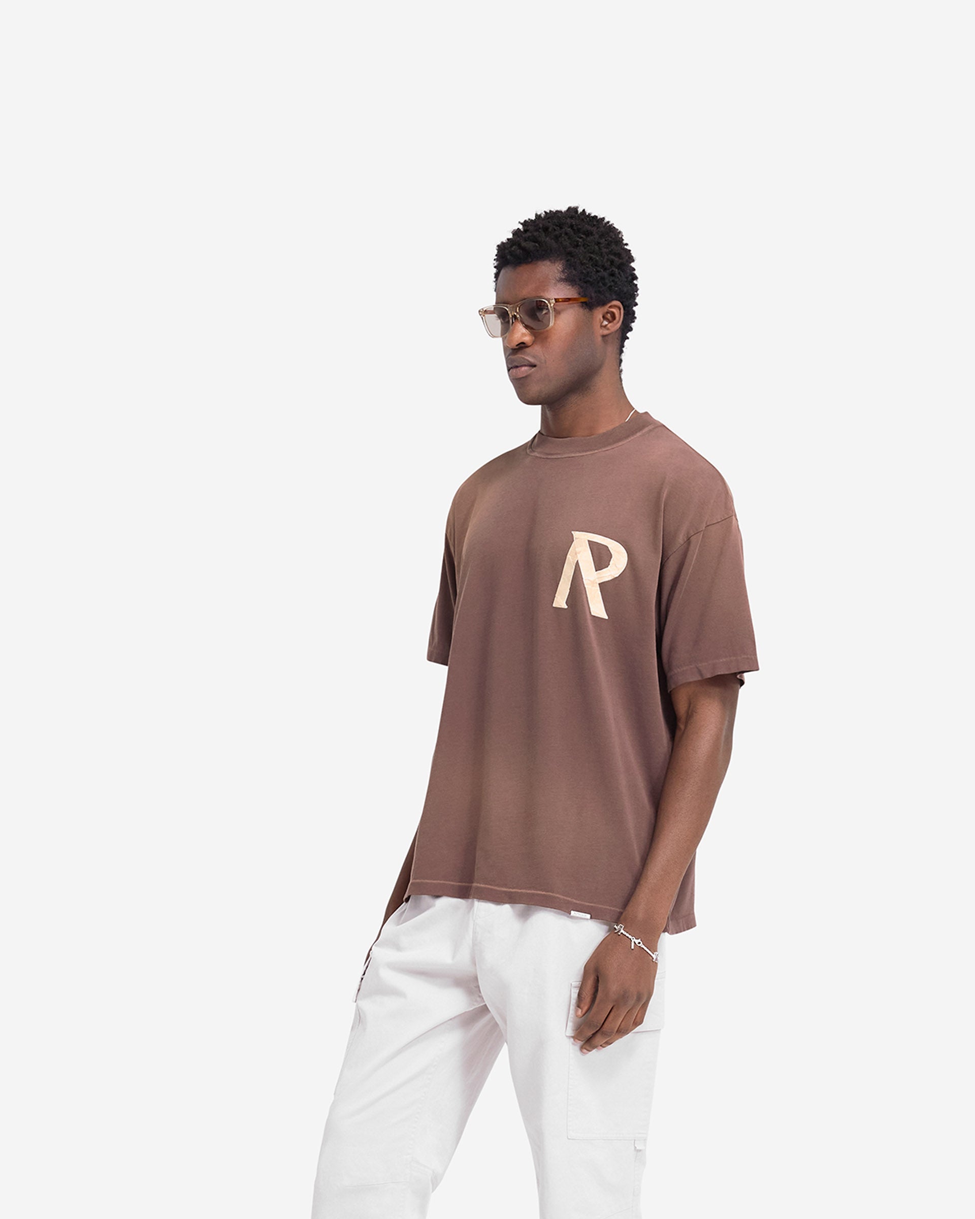 Man wearing a brown t-shirt on a plain white background | Masking Tape Initial T-Shirt in Cedar | Slightly oversized t-shirt with 3D masking tape effect initial | FW24 T-Shirts | Represent Clo