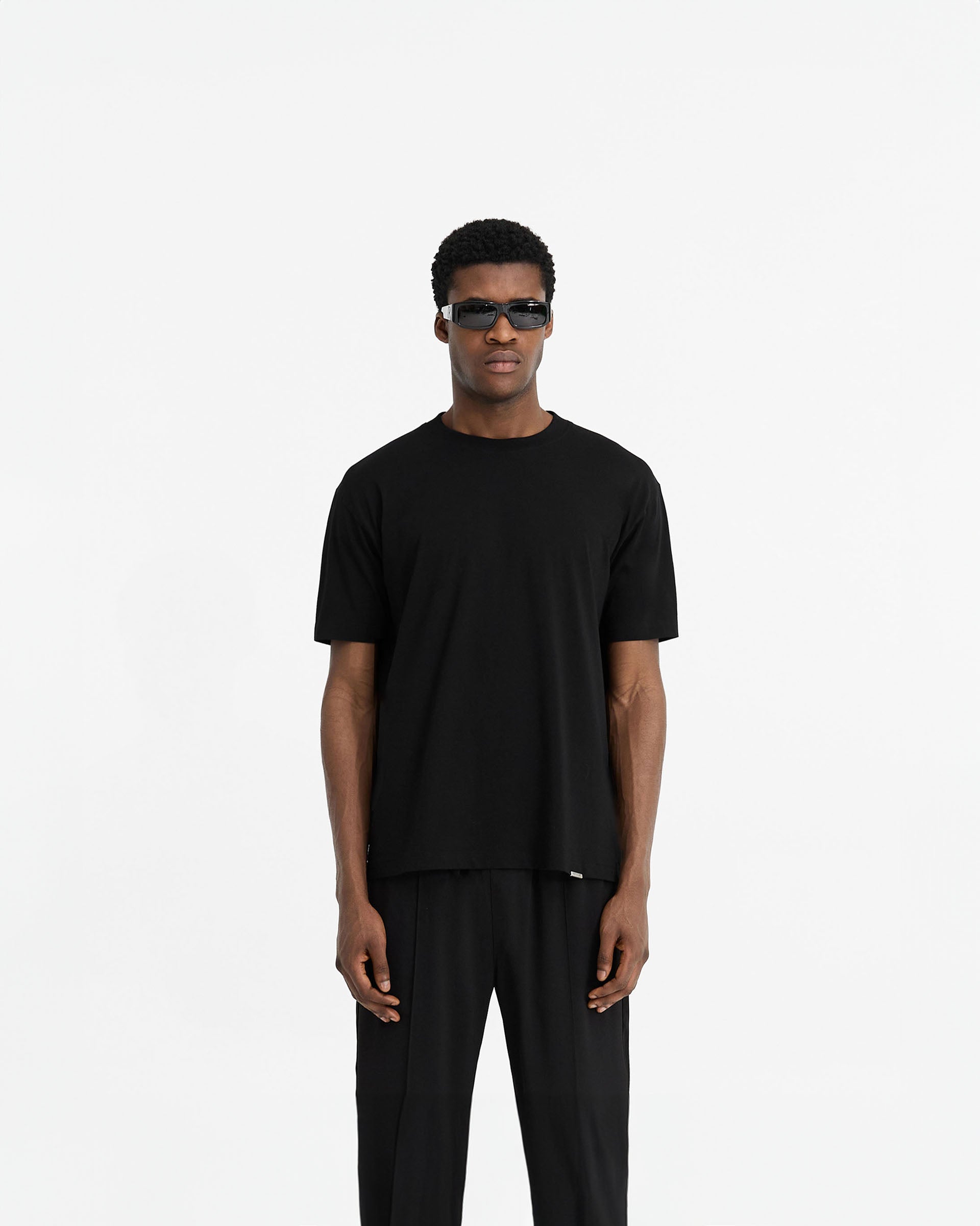 Man wearing a black t-shirt on a plain white background | Initial T-Shirt in Black | Slim fit t-shirt with embroidered Initial and metal bar logo | Initial T-Shirts | Represent Clo