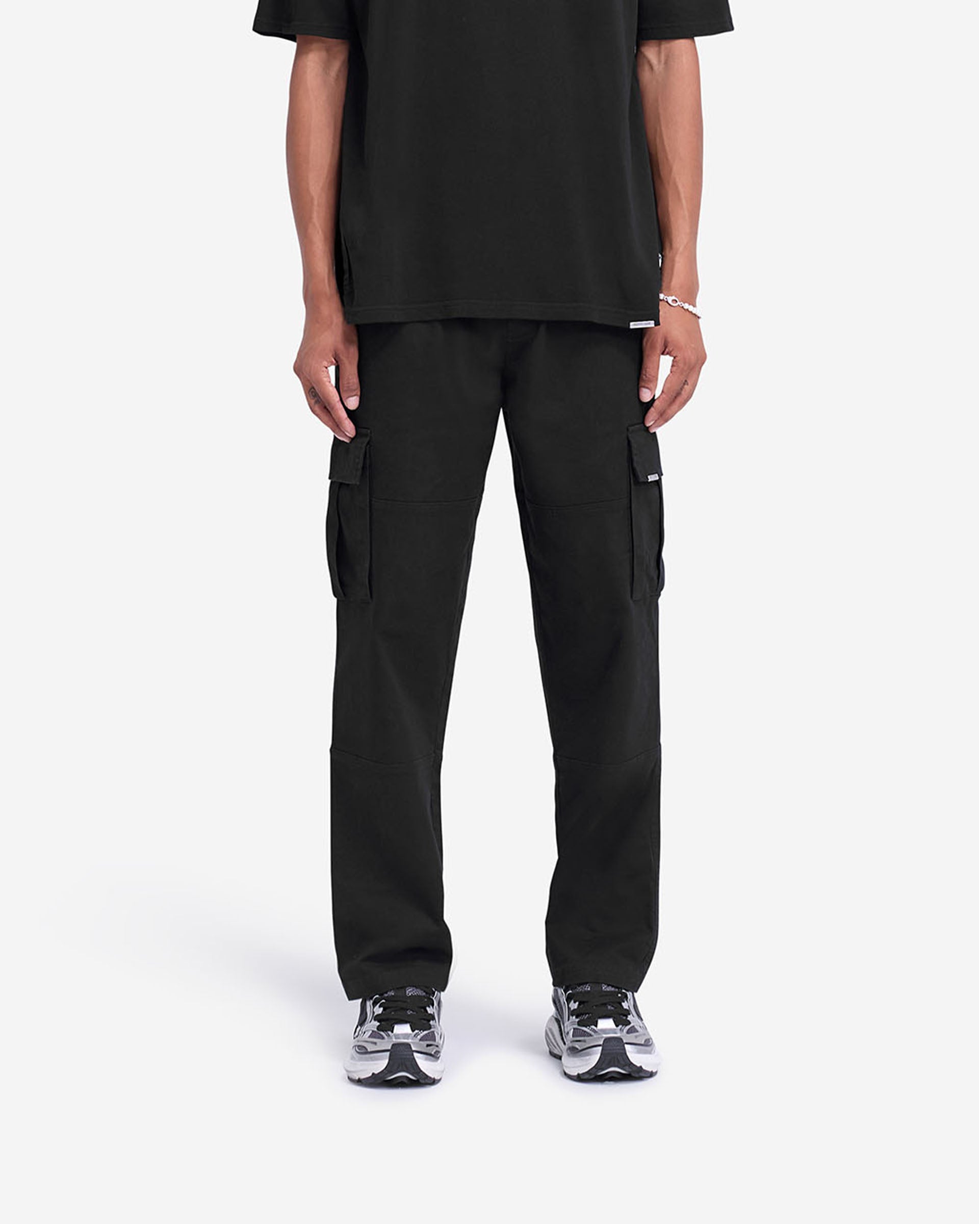 Man wearing black cargo pants on a plain white background | Cargo Pant in Black | Cargo pants with elasticated waistband and flap pockets | FW24 Pants | Represent Clo