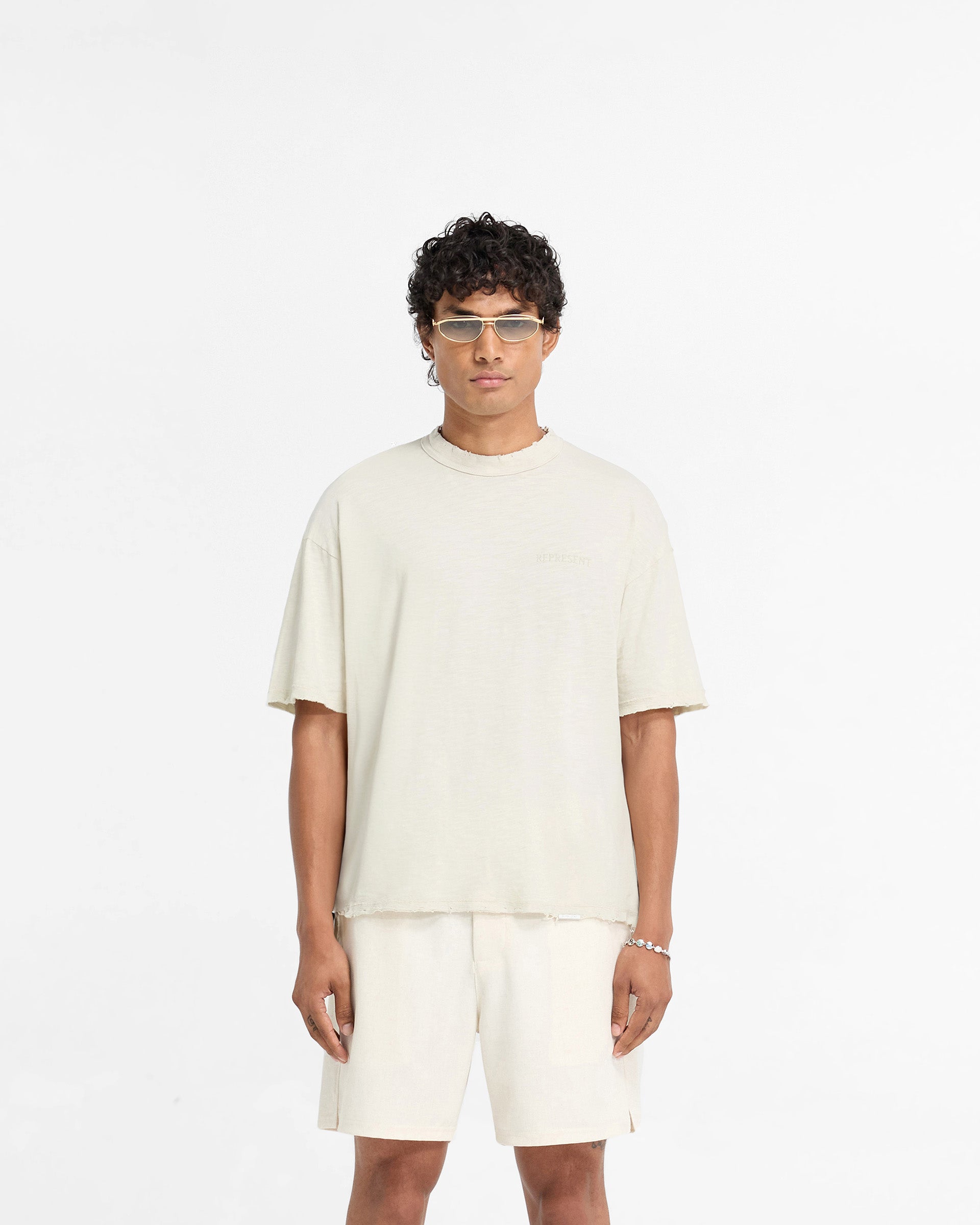 Man wearing a white t-shirt on a plain white background | Slub T-Shirt in White Sand | Oversized fit t-shirt with tonal embroidered branding | FW24 T-Shirts | Represent Clo
