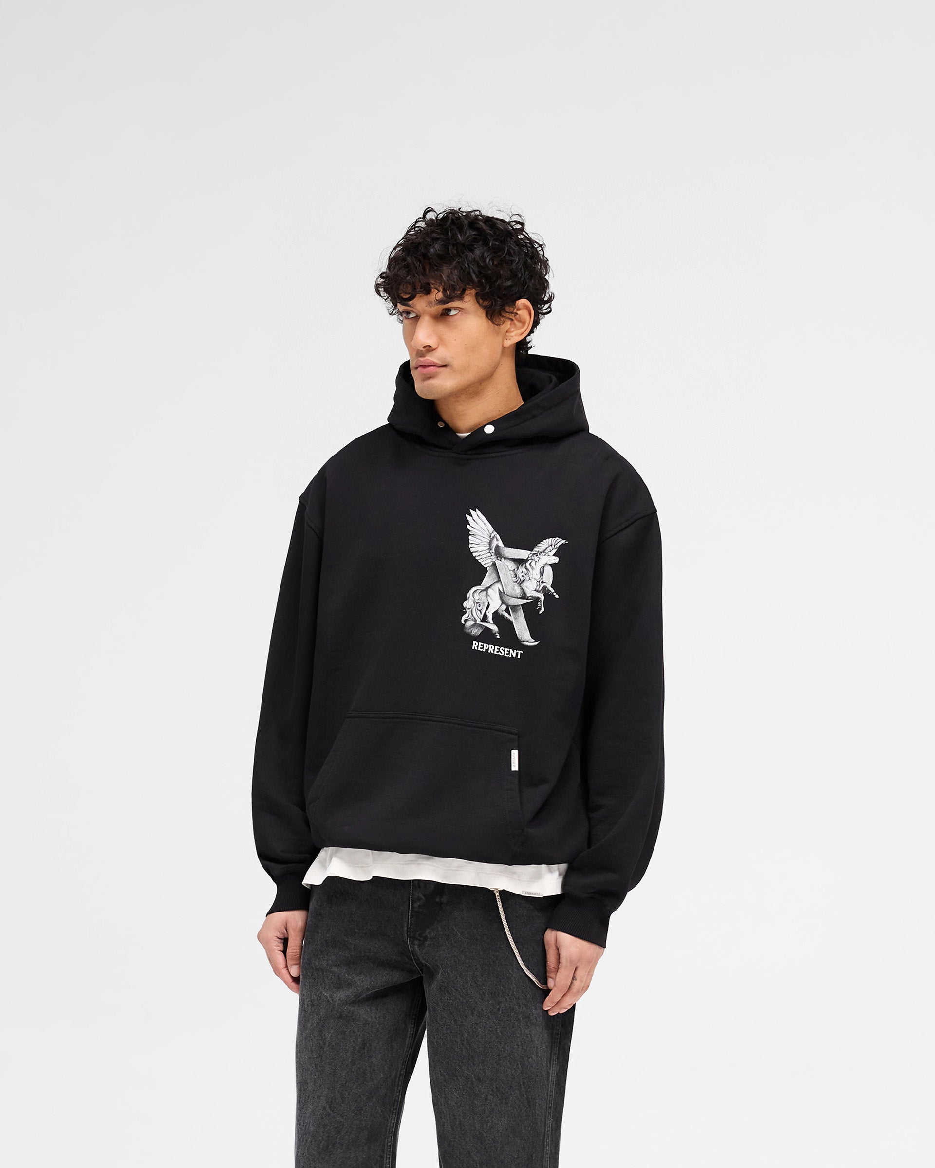 Man wearing a black hoodie on a plain white background | Elegance In Motion Hoodie in Jet Black | Oversized hoodie with motion graphic and popper fastening | SS25 Hoodies | Represent Clo