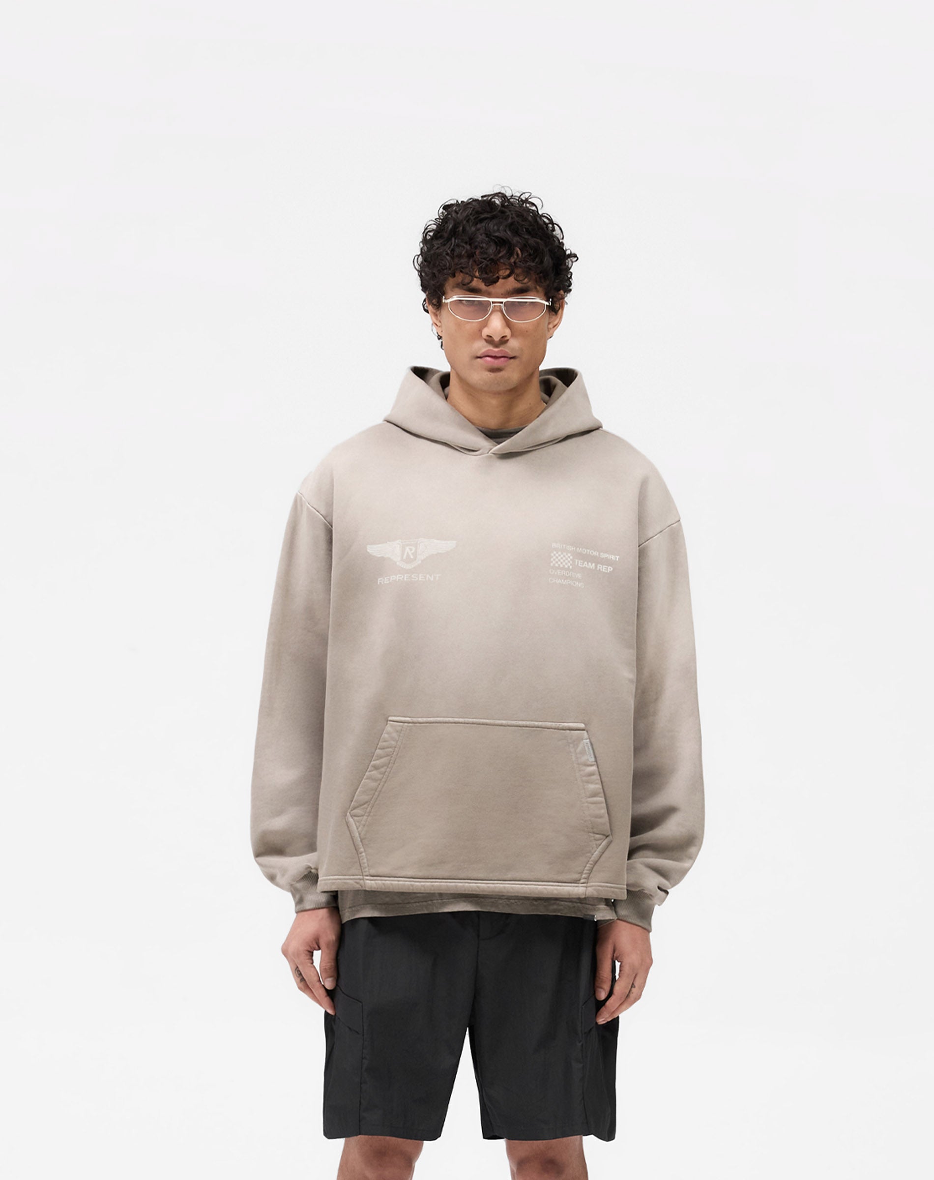 Man wearing an oversized dark taupe hoodie on a plain white background | Team Rep Hoodie in Dark Taupe | Heavy weight jersey cotton hoodie with vintage graphic | SS25 Hoodies | Represent Clo