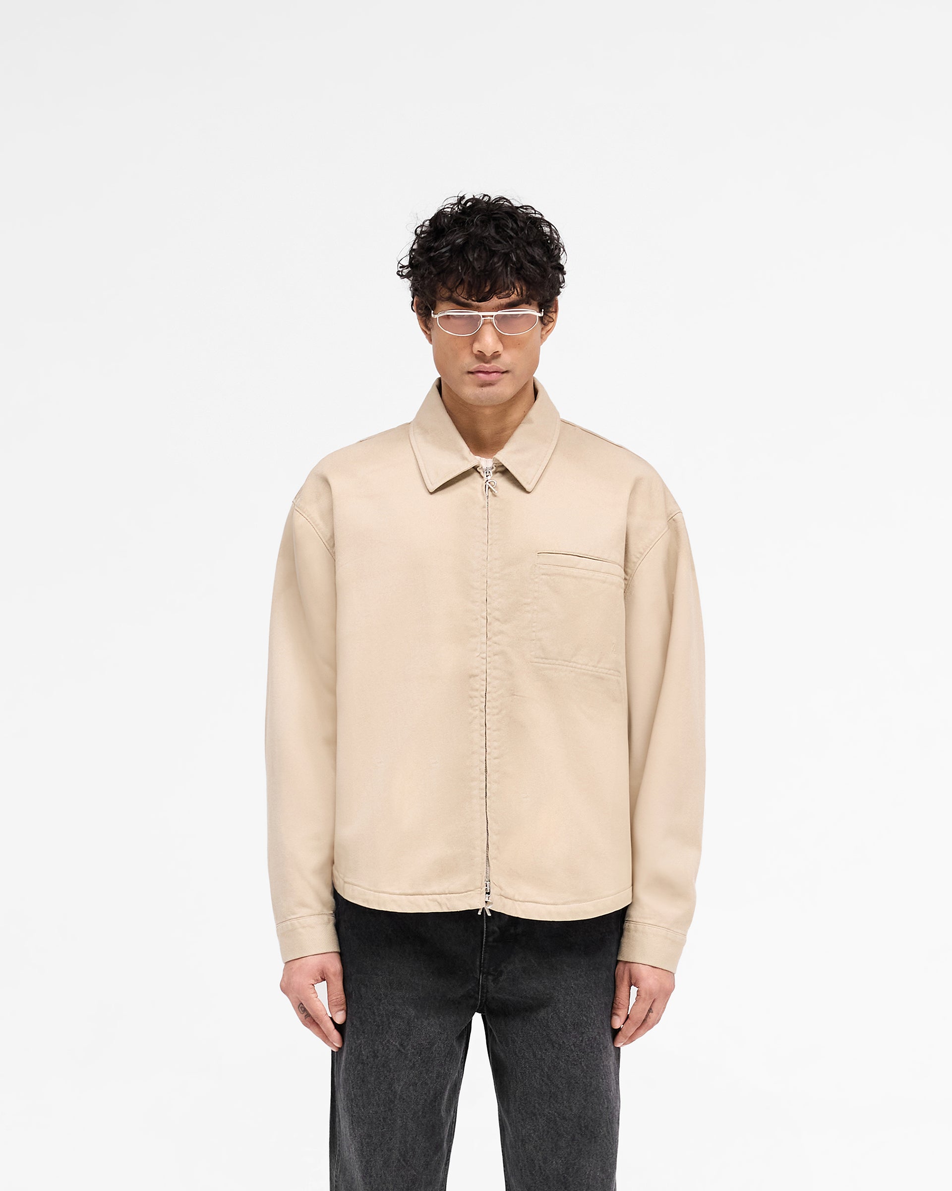 Man wearing a beige zip-through cotton shirt on a plain white background | Cotton Zip Through Shirt in Beige | Structured fit cotton twill shirt with double Represent zips and chest pocket | SS25 Shirts | Represent Clo