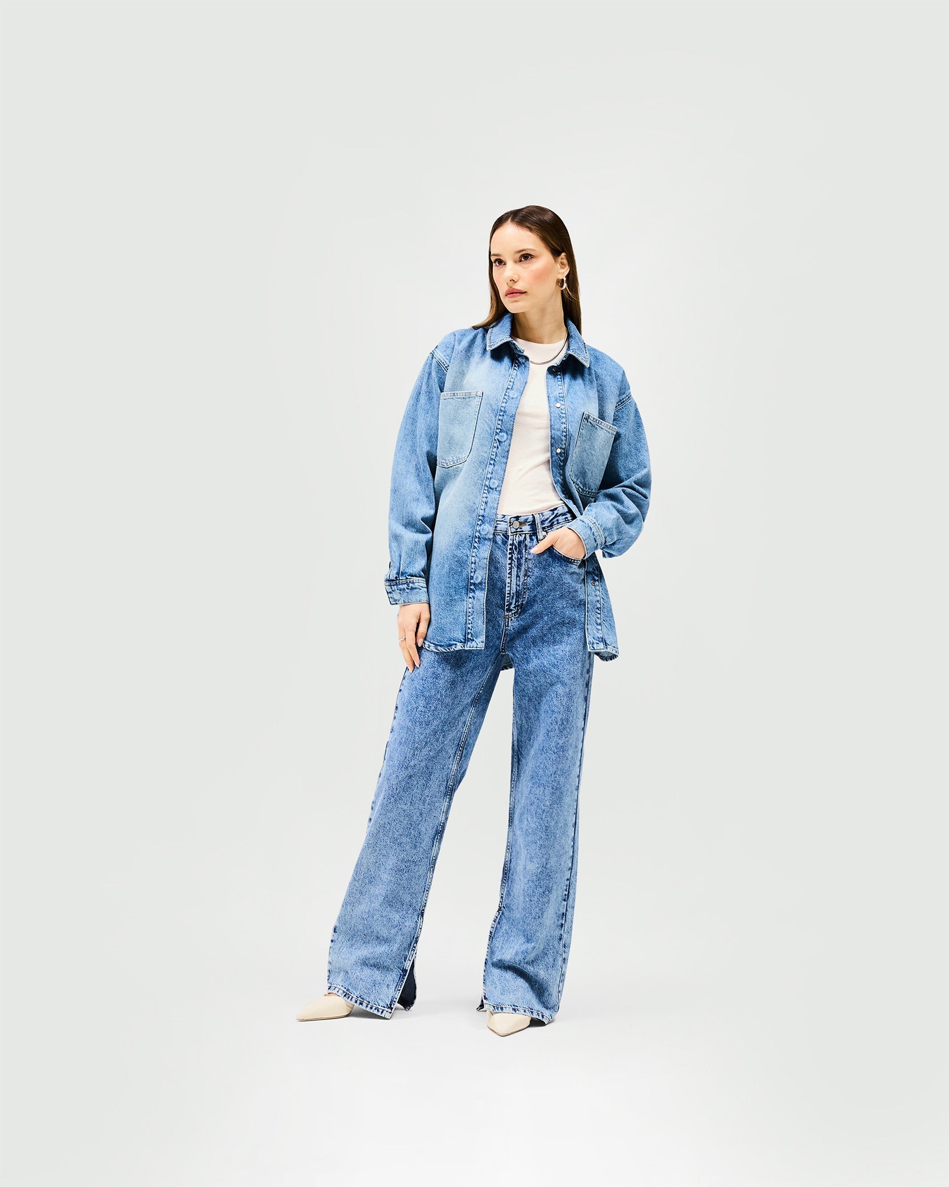 Woman wearing an oversized blue denim overshirt on a plain white background | Denim Overshirt in Washed Blue | Oversized fit denim shirt with popper fastening | Womens SS25 Denim | Represent Clo