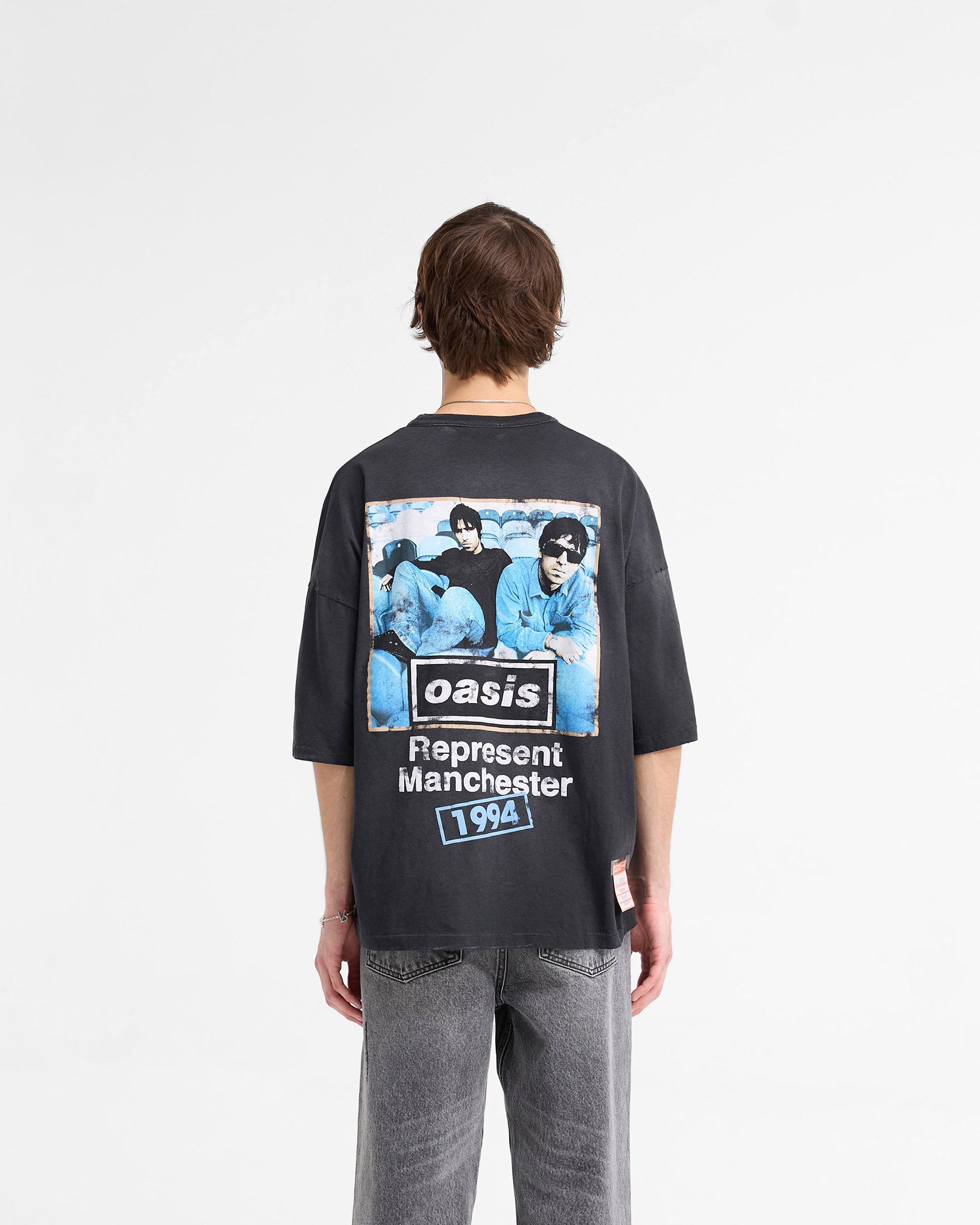 Man wearing a black t-shirt with Oasis imagery on a plain white background | Represent X Oasis Maine Road T-Shirt in Washed Black | Oversized boxy t-shirt with distressed details | FW24 T-Shirts | Represent Clo