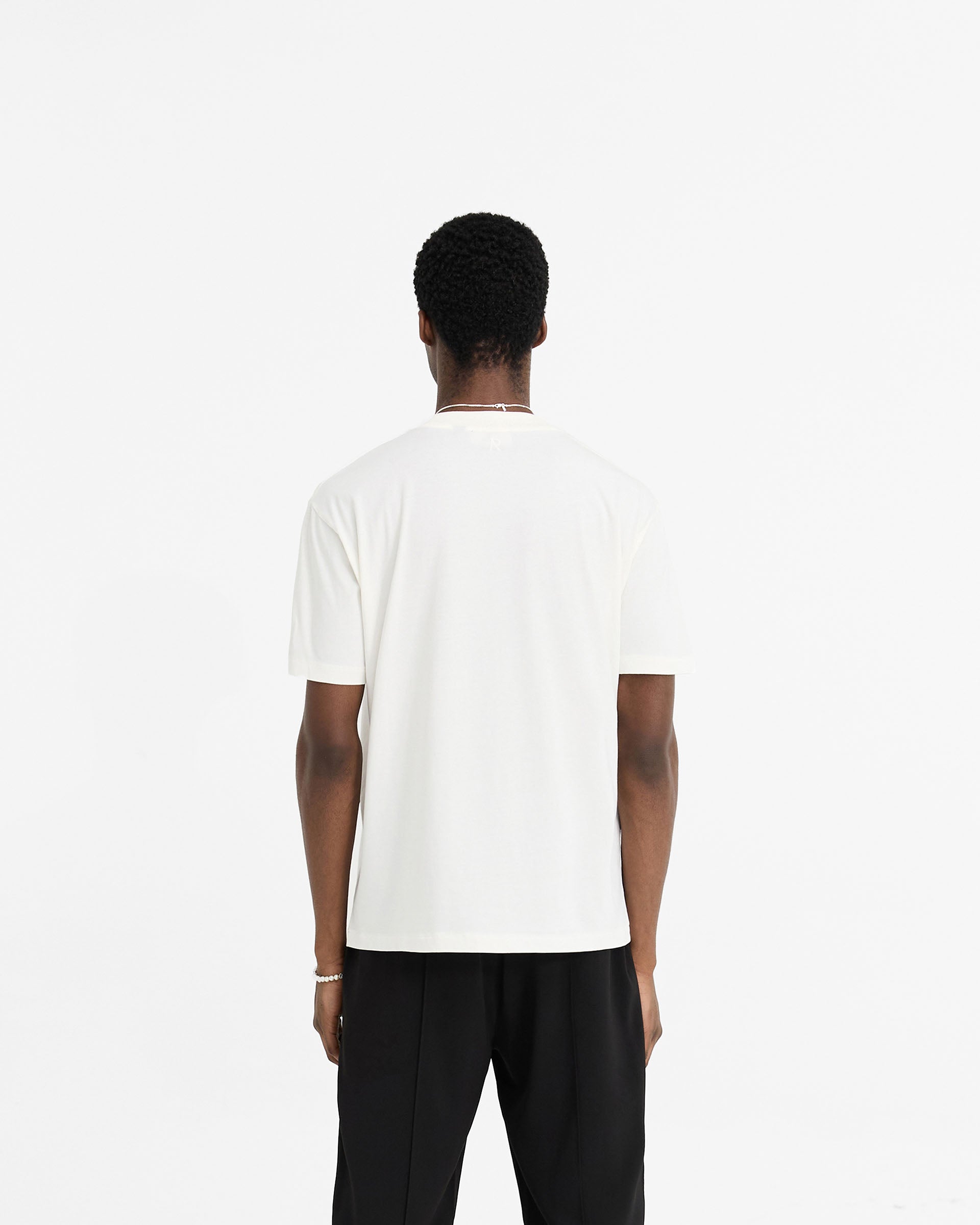 Man wearing a white t-shirt on a plain white background | Initial T-Shirt in Flat White | Regular fit t-shirt with embroidered initial and metal bar logo | Initial T-Shirts | Represent Clo