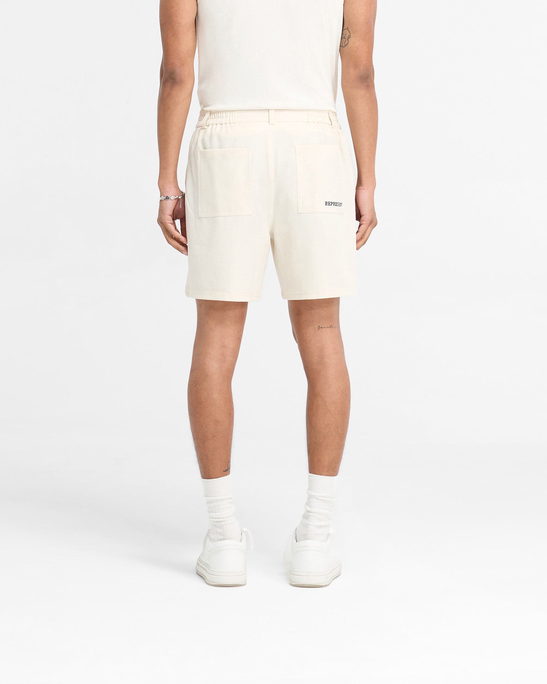 Man wearing mens white shorts on a plain white background | Logo Yacht Short in Antique White | Yacht shorts with hybrid waistband and side splits | FW24 Shorts | Represent Clo
