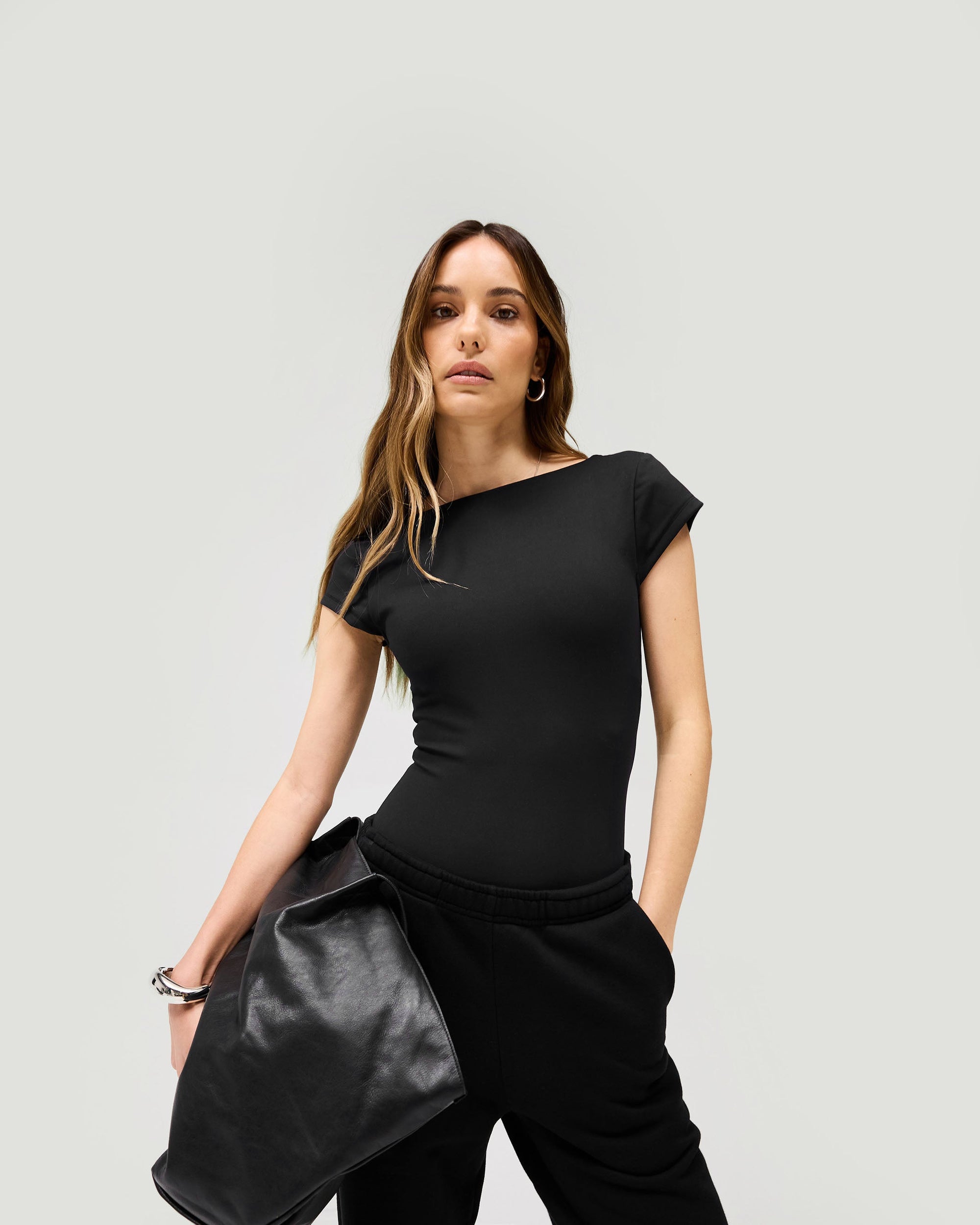 Woman wearing a black bodysuit on a plain white background | Owners Club Bodysuit in Jet Black | Sculpting bodysuit with low scoop back and cap sleeves | Womens Owners Club Tops | Represent Clo