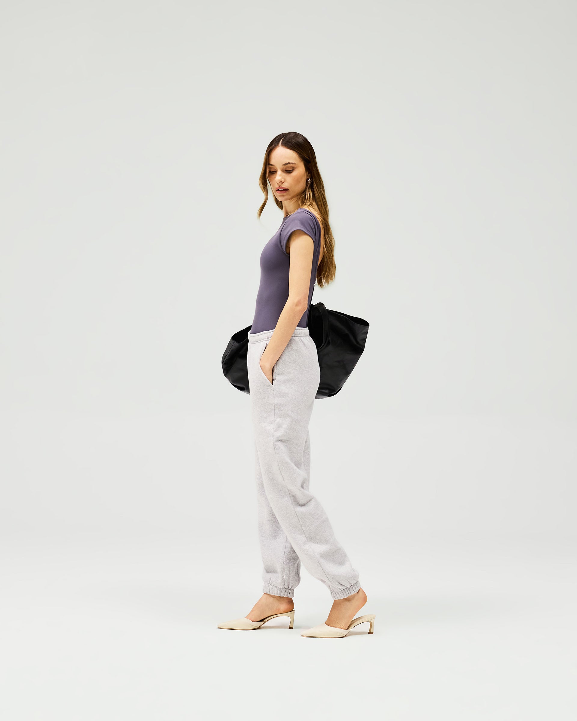Woman wearing grey track pants on a plain white background | Owners Club Track Pant in Grey Marl | Relaxed fit track pants with elasticised waist and hem cuffs | Womens Owners Club Bottoms | Represent Clo