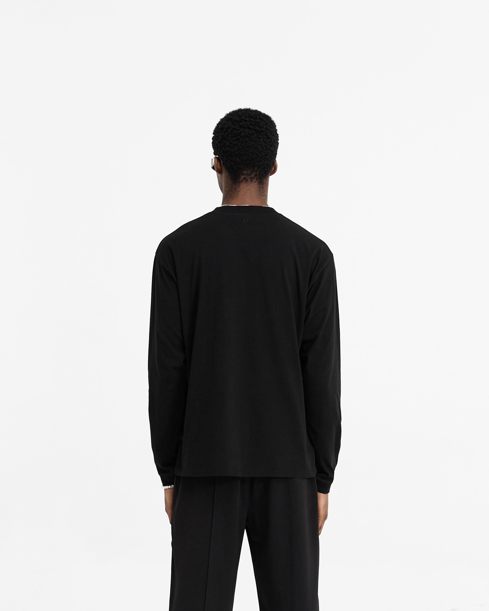 Man wearing a black long sleeve t-shirt on a plain white background | Initial Long Sleeve T-Shirt in Black | Regular fit long sleeve t-shirt with embroidered details | Initial T-Shirts | Represent Clo