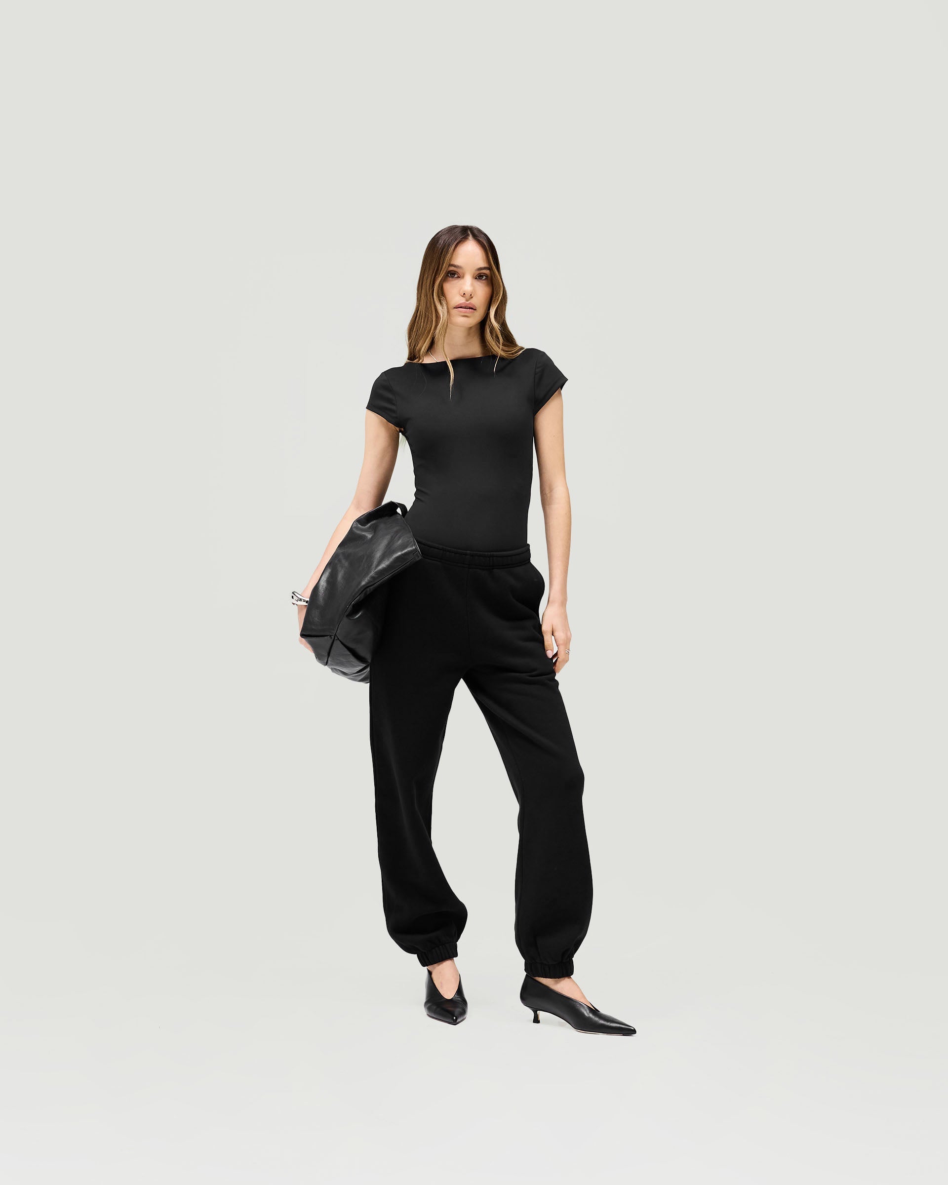 Woman wearing a black bodysuit on a plain white background | Owners Club Bodysuit in Jet Black | Bodysuit with low scoop back and cap sleeves | Womens Owners Club Tops | Represent Clo