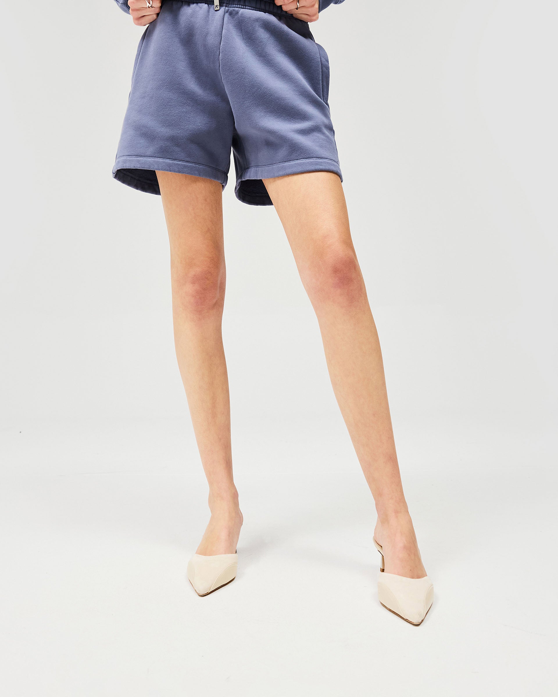 Woman wearing steel blue shorts on a plain white background | Owners Club Short in Steel Blue | Mid rise sweat shorts with elasticised leg hem cuffs | Womens Owners Club Shorts | Represent Clo