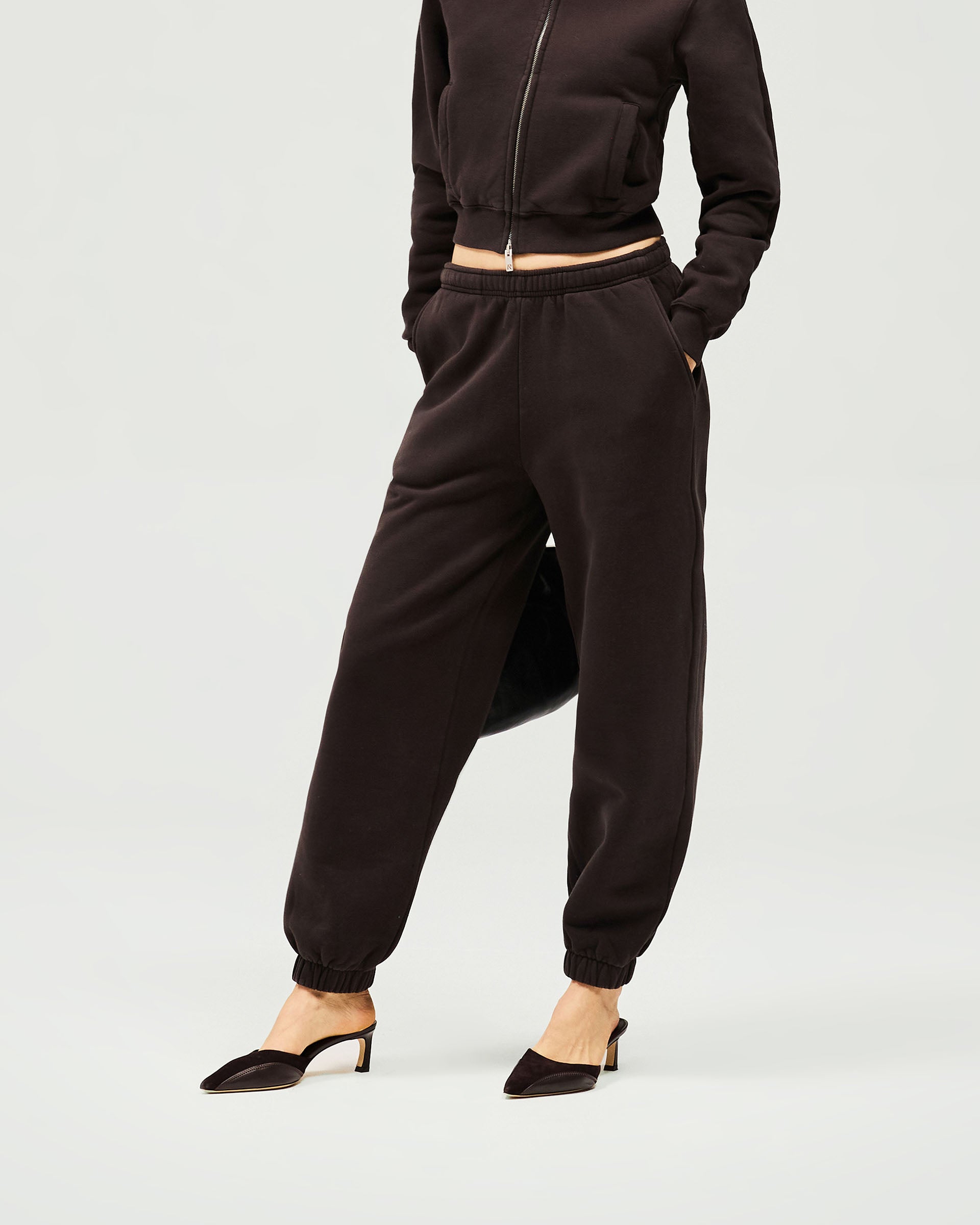 Woman wearing black track pants on a plain white background | Owners Club Track Pant in Black Coffee | Sweatpants with drawcord and side pockets | Womens Owners Club Bottoms | Represent Clo