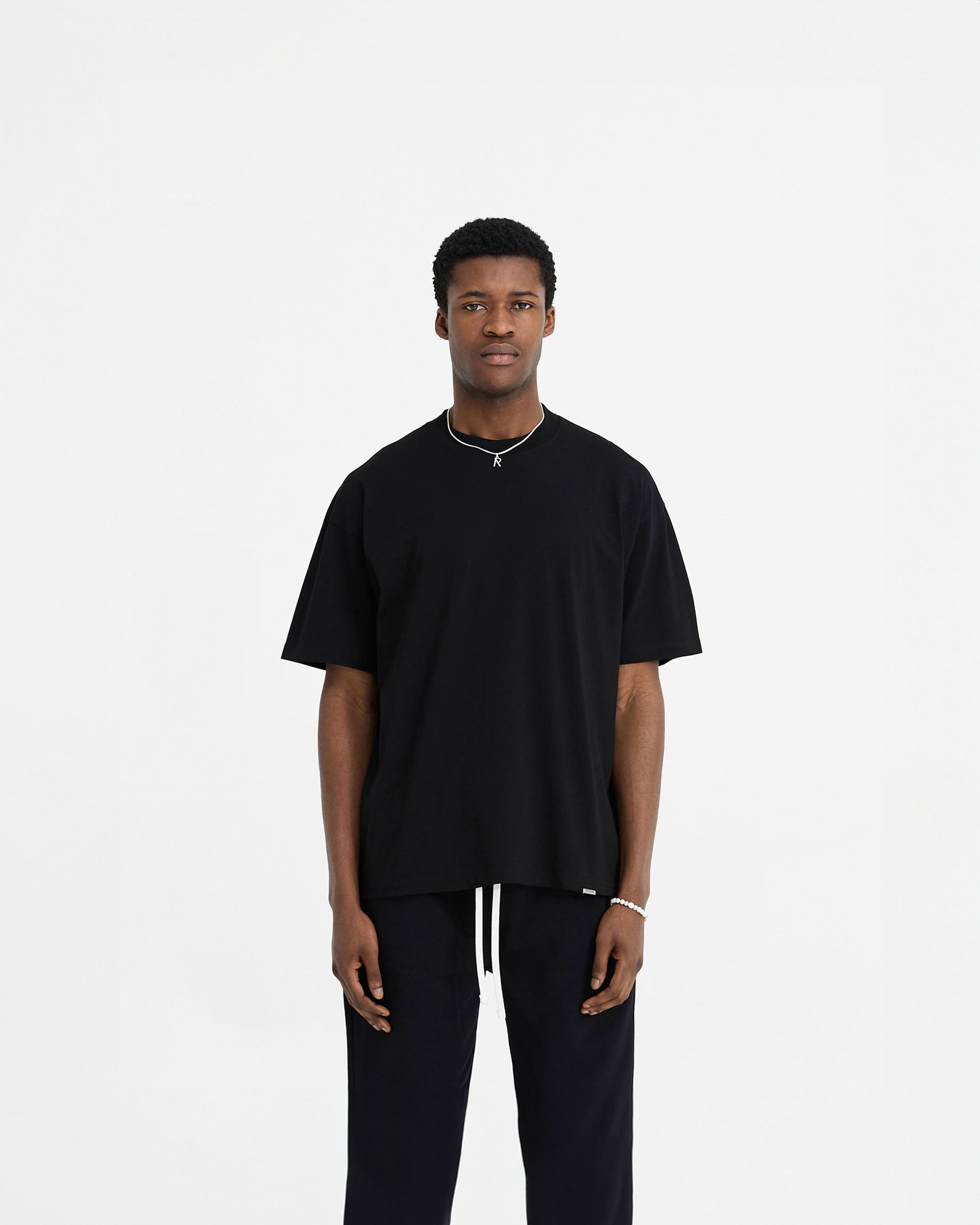 Man wearing a black oversized t-shirt on a plain white background | Initial Oversized T-Shirt in Black | Oversized t-shirt with embroidered details | Initial T-Shirts | Represent Clo