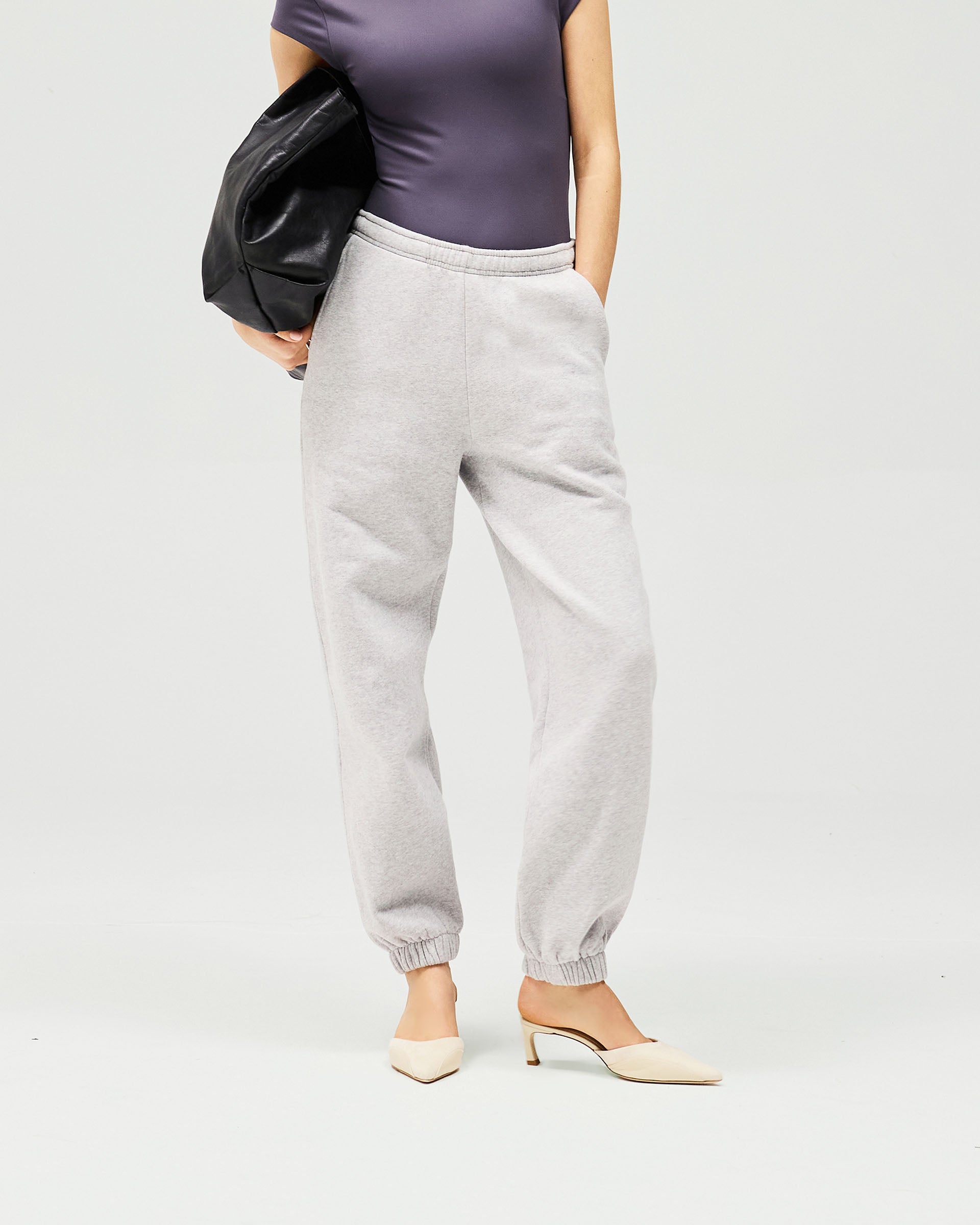 Woman wearing relaxed grey track pants on a plain white background | Owners Club Track Pant in Grey Marl | Sweatpants with elasticised leg cuffs | Womens Owners Club Bottoms | Represent Clo