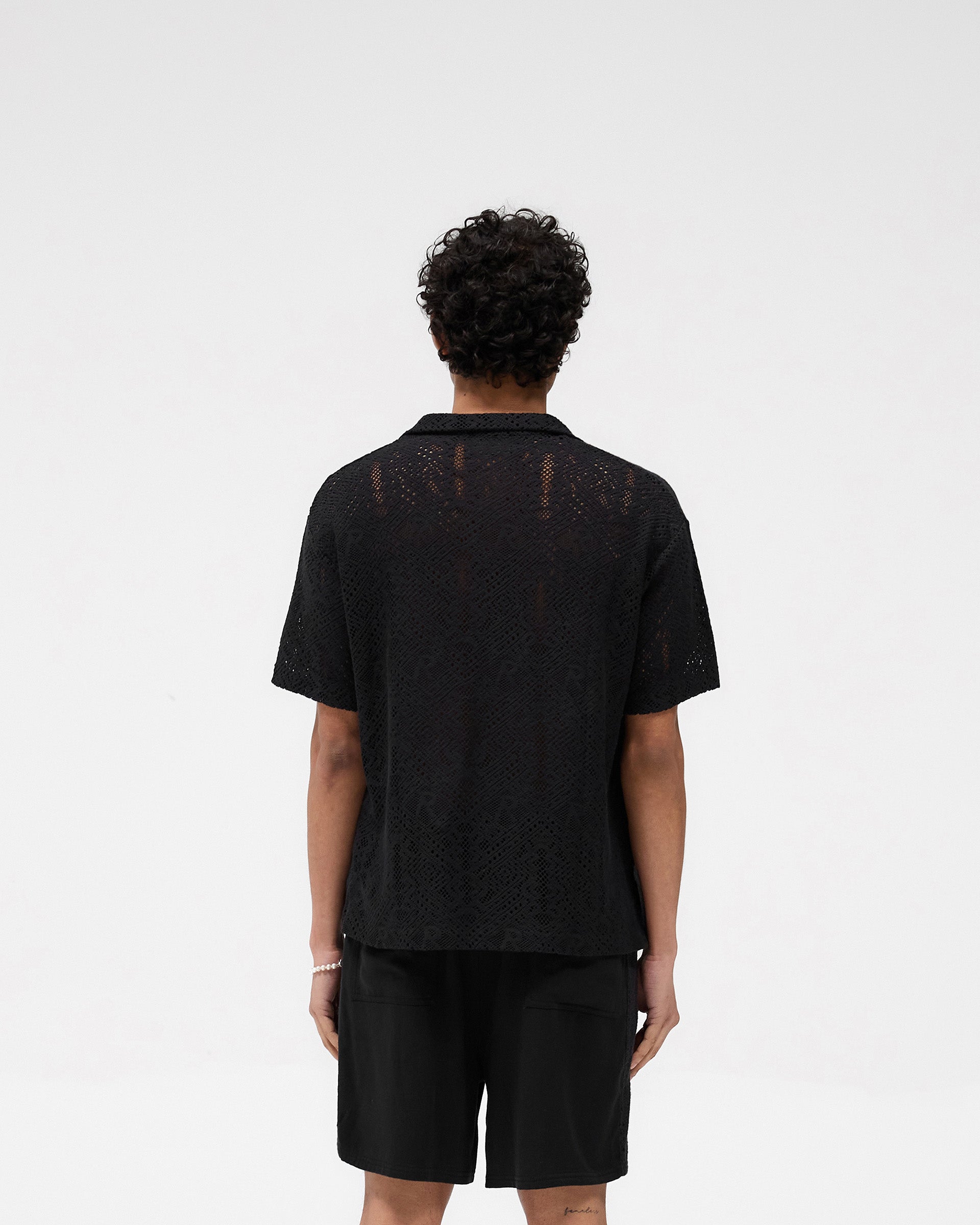 Man wearing a black crochet shirt on a plain white background | All Over Crochet Shirt in Jet Black | Oversized fit crochet shirt with camp collar | SS25 Knitwear | Represent Clo