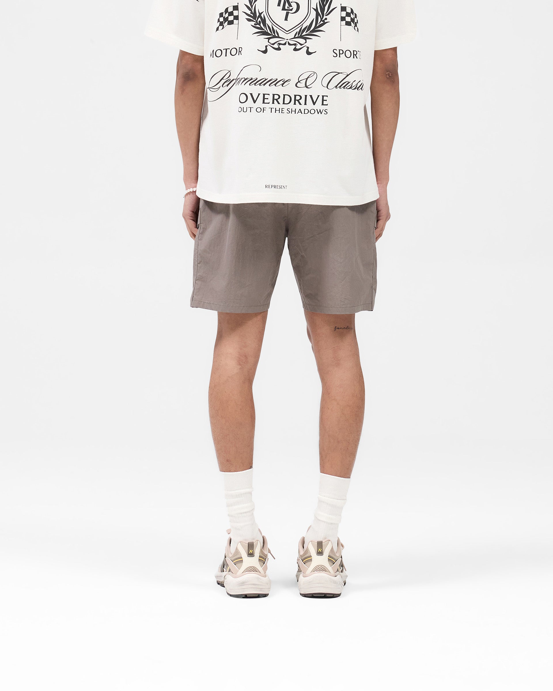 Man wearing mid grey shorts on a plain white background | Tech Cargo Short in Mid Grey | Lightweight woven fabric shorts with pleated cargo pockets | SS25 Shorts | Represent Clo