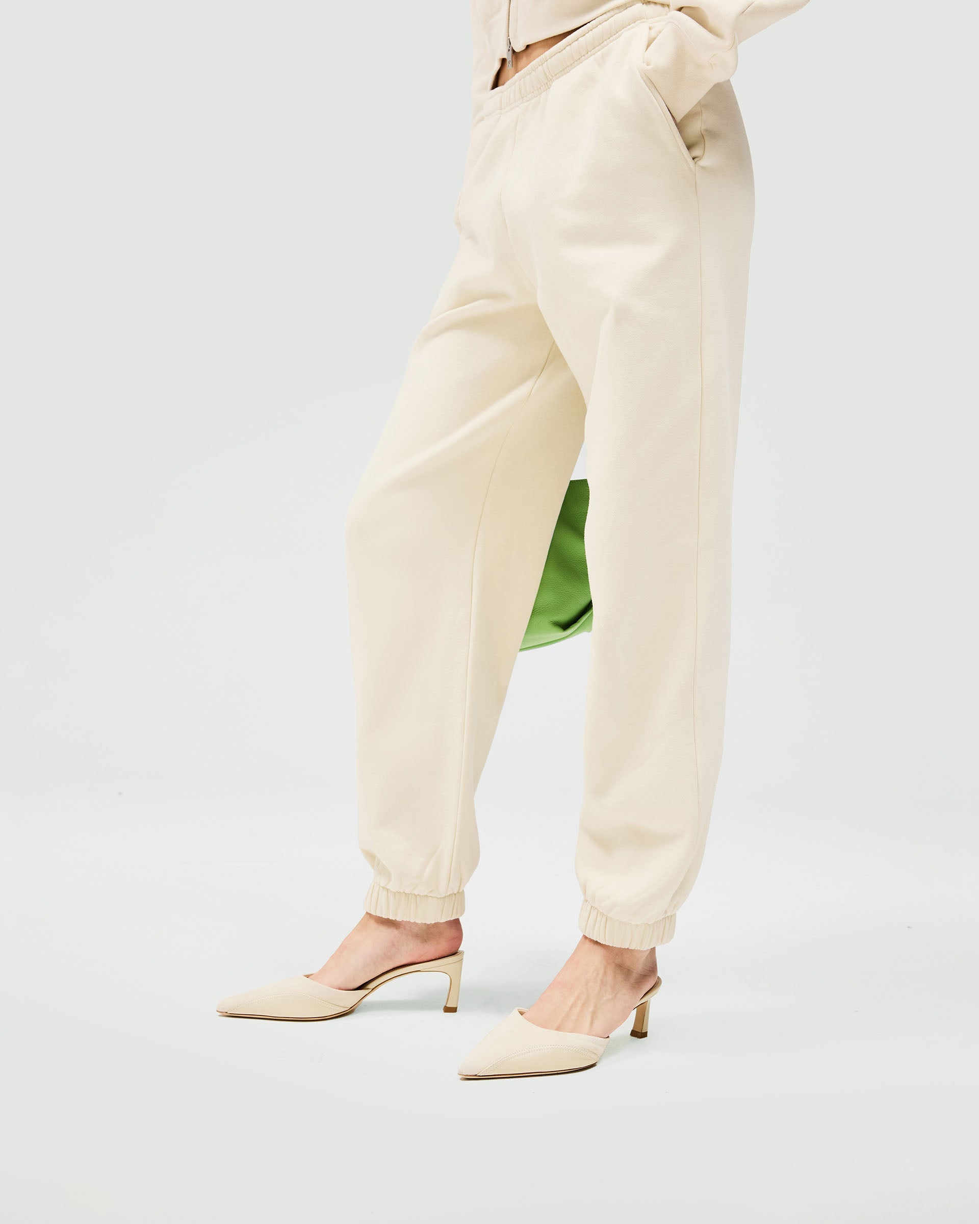 Woman wearing cream track pants on a plain white background | Owners Club Track Pant in Oat Milk | Sweatpants with elasticised waistband and leg cuffs | Womens Owners Club Bottoms | Represent Clo