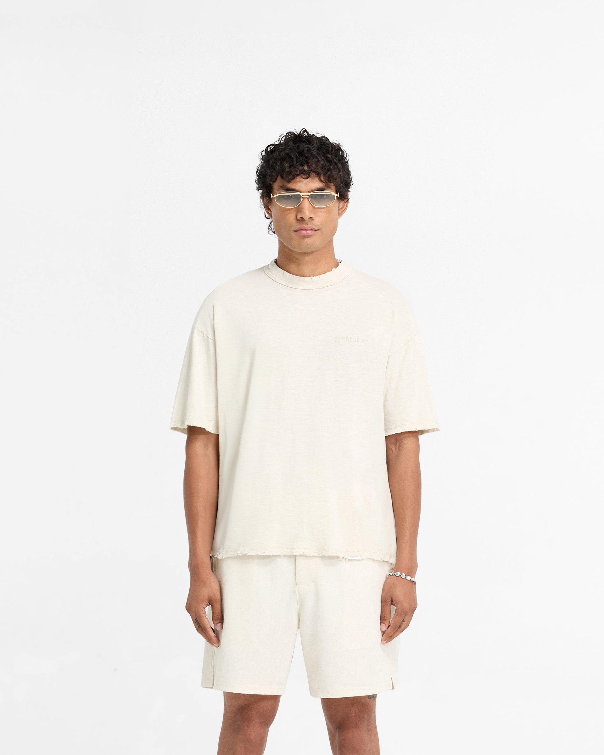 Man wearing an oversized white t-shirt on a plain white background | Slub T-Shirt in Flat White | Distressed t-shirt with tonal embroidered branding | FW24 T-Shirts | Represent Clo