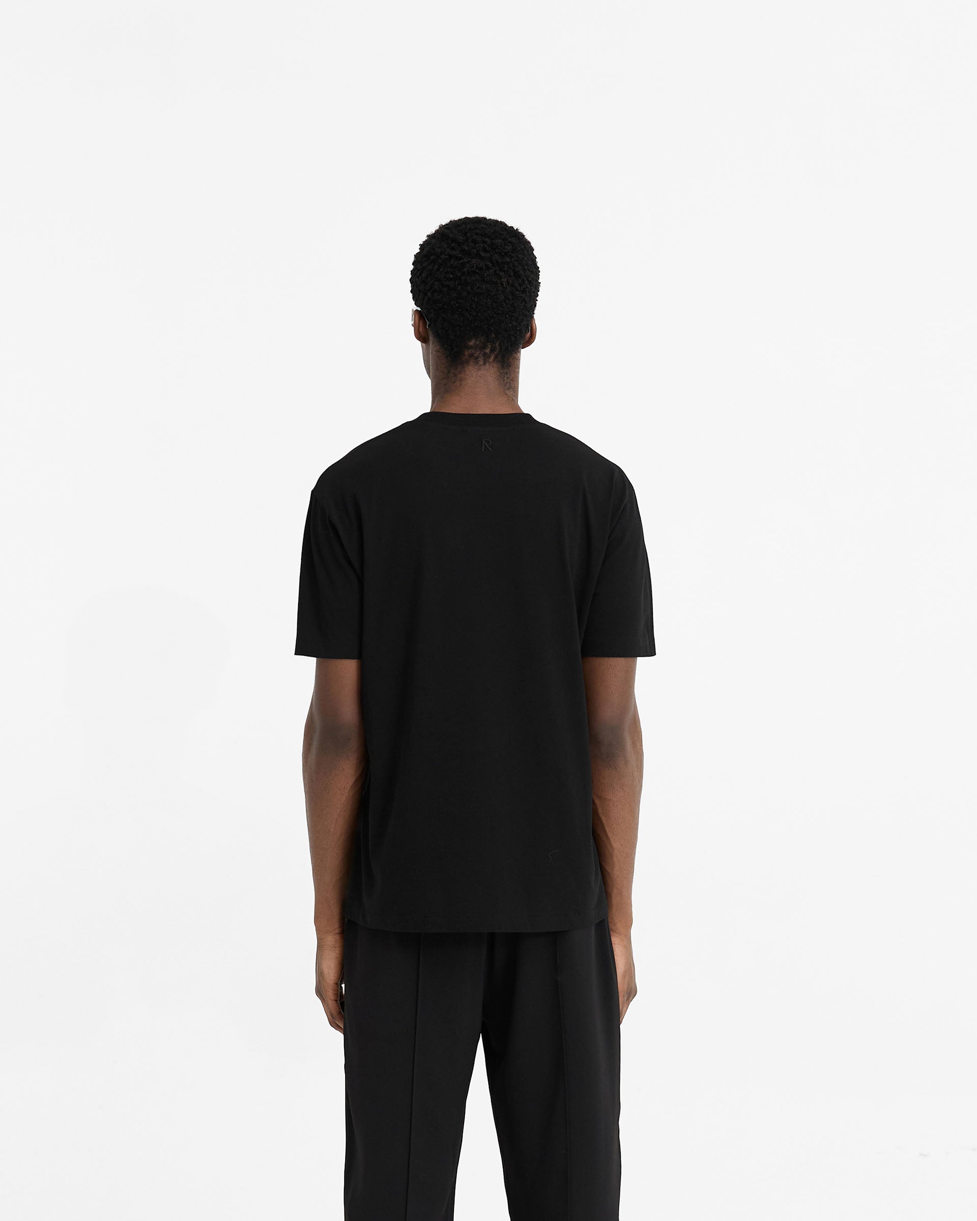 Man wearing a black t-shirt on a plain white background | Initial T-Shirt in Black | Regular fit tee with embroidered detail and 1x1 rib collar | Initial T-Shirts | Represent Clo