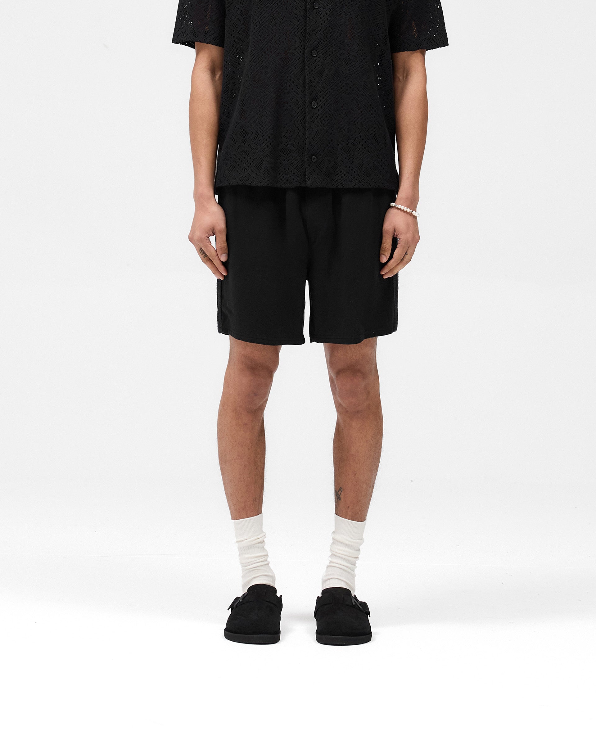 Man wearing black knitted panel shorts on a plain white background | Knitted Panel Short in Black | Relaxed fit shorts with knitted side detailing | SS25 Shorts | Represent Clo