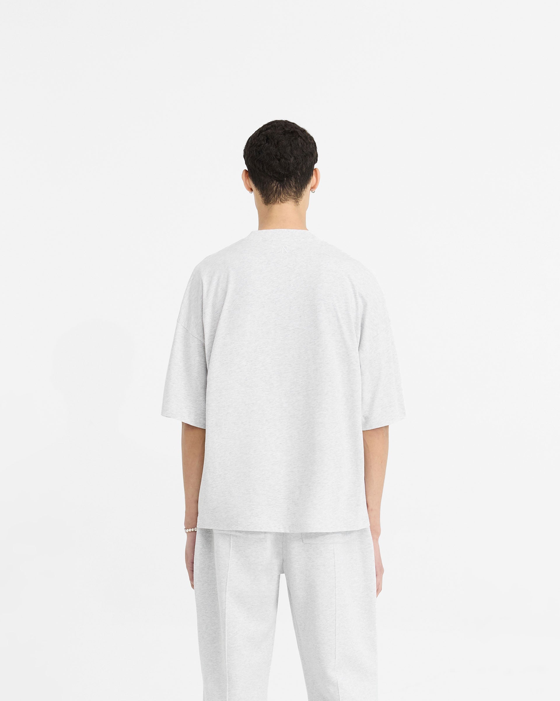 Man wearing a grey boxy t-shirt on a plain white background | Initial Boxy T-Shirt in Ice Grey Marl | Oversized cropped t-shirt with ribbed collar | Initial T-Shirts | Represent Clo
