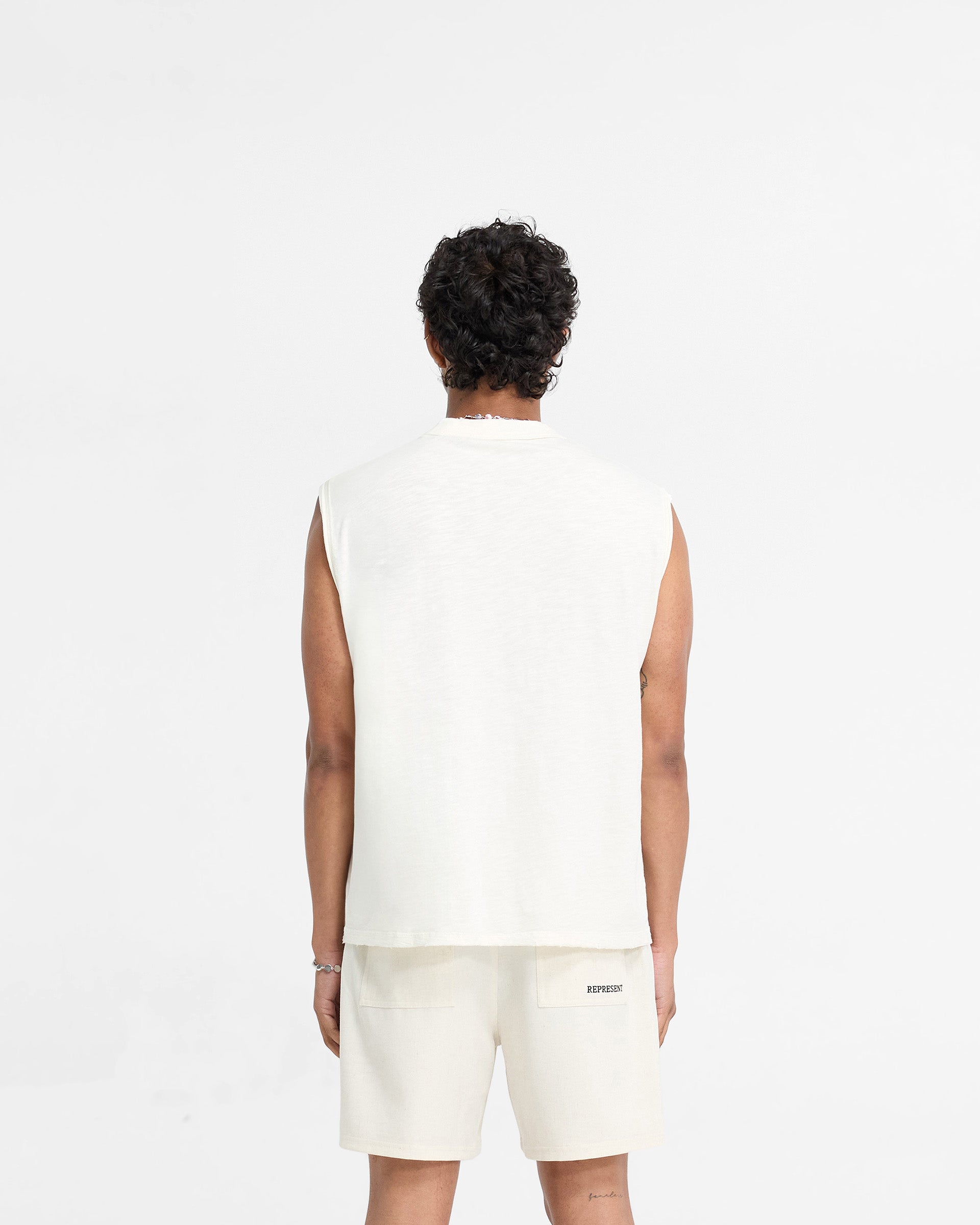 Man wearing a white tank top on a plain white background | Slub Tank in Flat White | Oversized cotton tank top with tonal embroidery | FW24 T-Shirts | Represent Clo