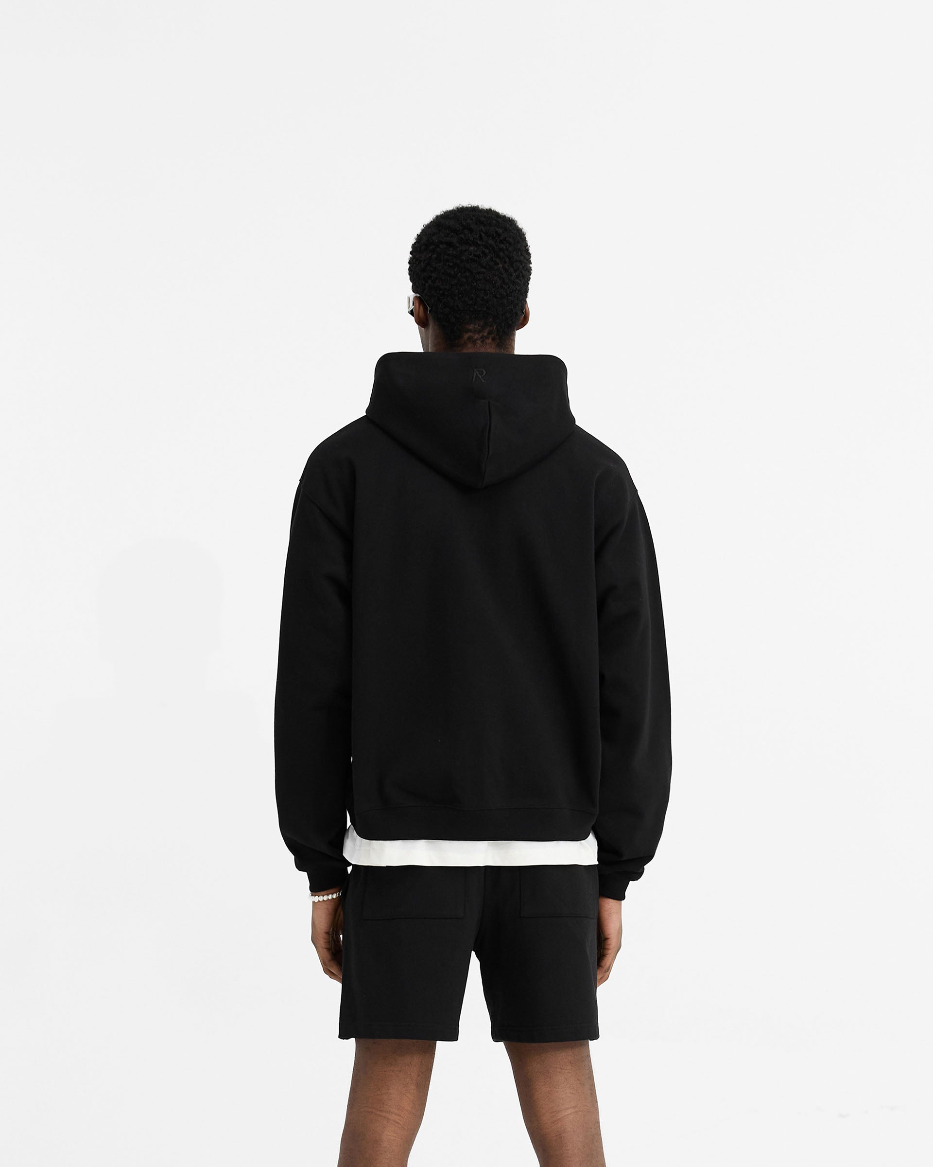 Man wearing a black oversized zip hoodie on a plain white background | Initial Oversized Zip Hoodie in Black | Heavyweight loopback jersey cotton hoodie with side seam pockets | Initial Hoodies | Represent Clo