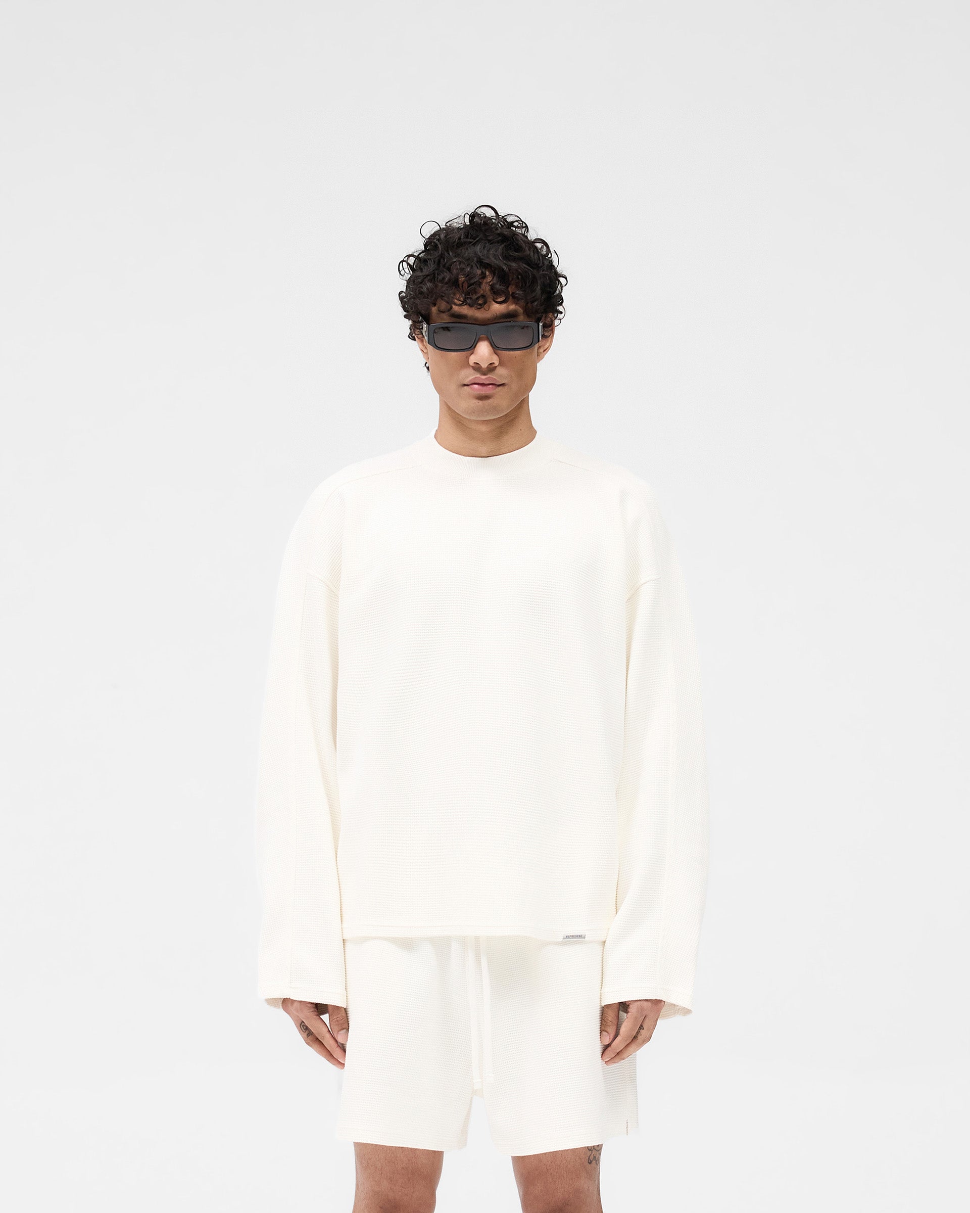 Man wearing a white long sleeve t-shirt on a plain white background | Waffle Long Sleeve T-Shirt in Flat White | Boxy fit waffle fabric t-shirt | SS25 T-Shirts | Represent Clo
