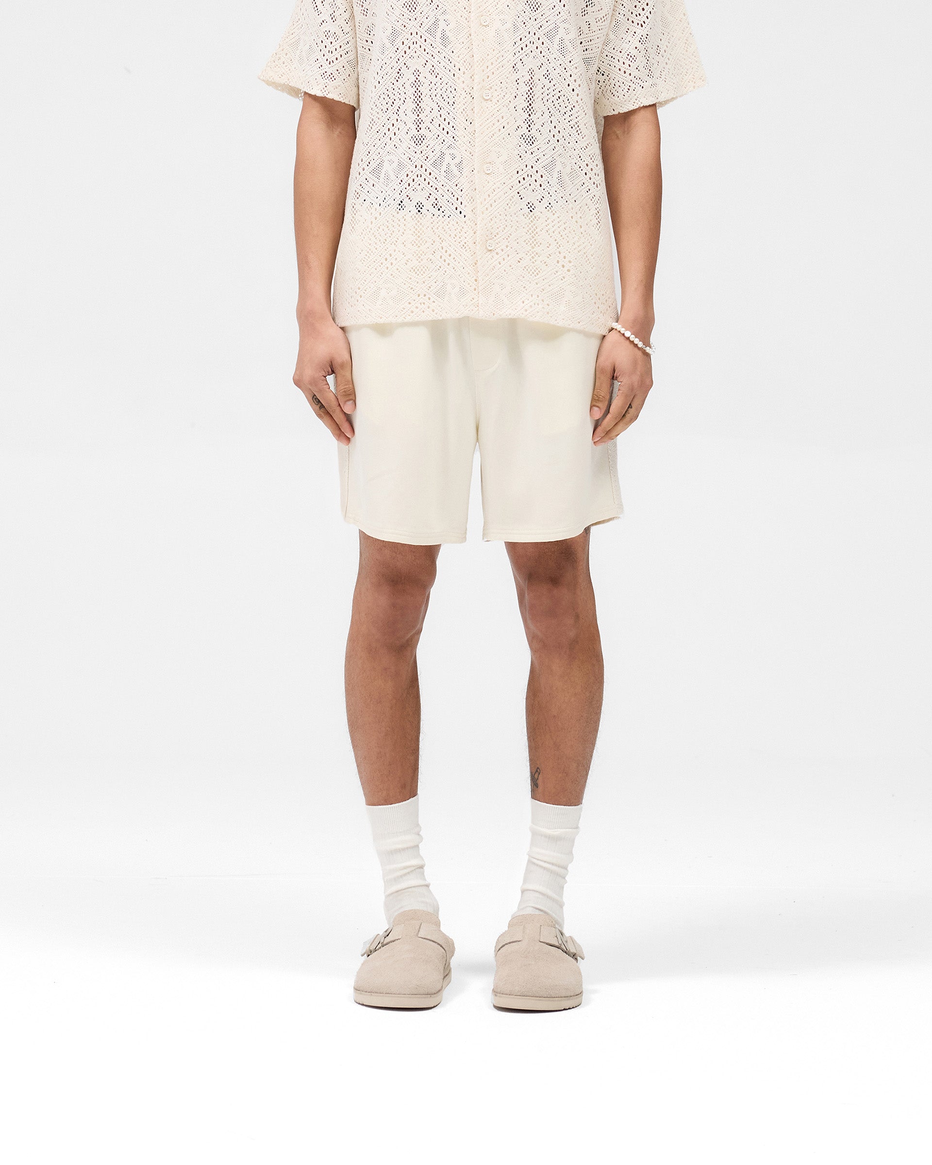 Man wearing antique white shorts on a plain white background | Knitted Panel Short in Antique White | Shorts with knitted panel detailing and elasticated waistband | SS25 Shorts | Represent Clo