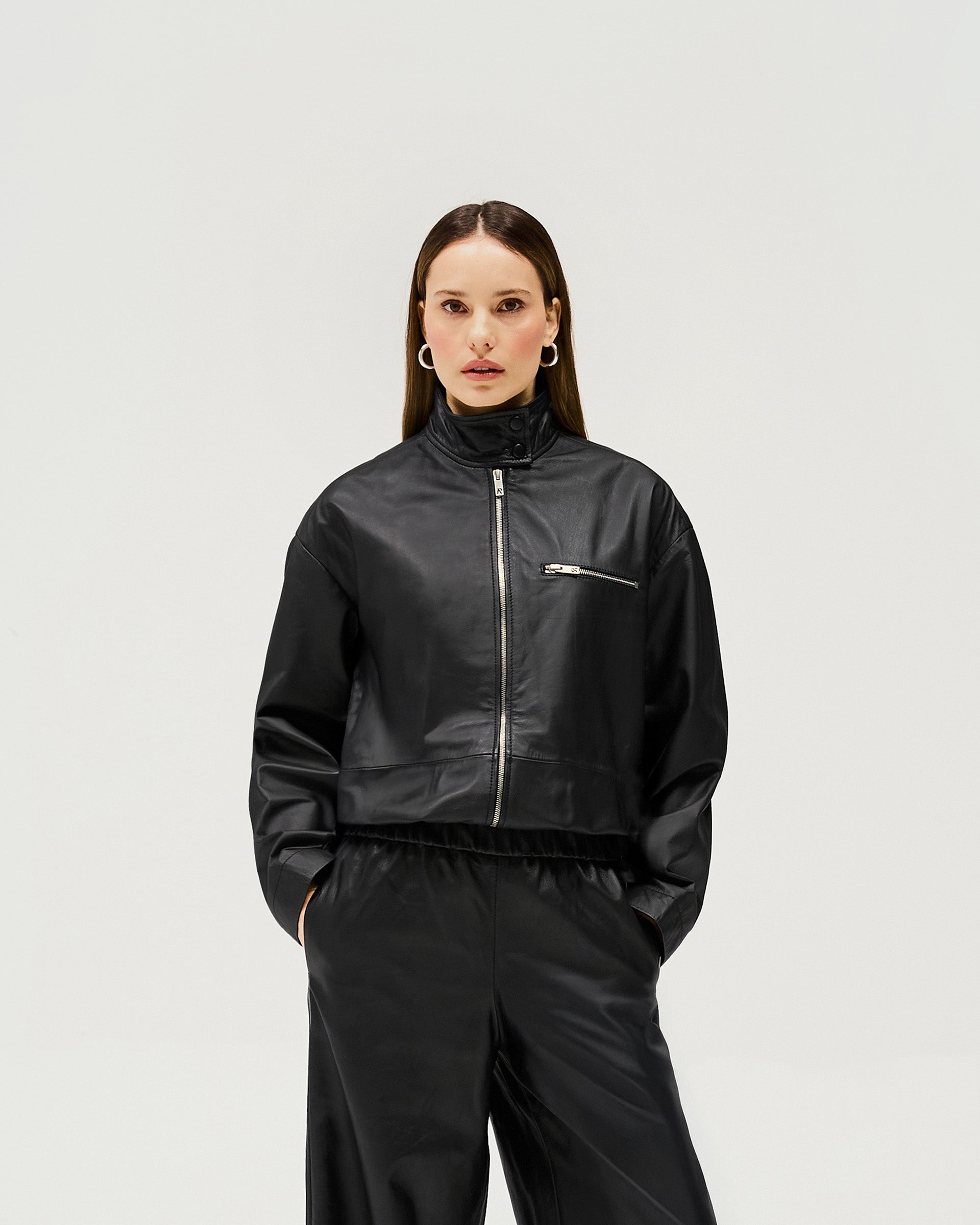 Woman wearing a black leather jacket on a plain white background | Fuel Jacket in Jet Black | Leather jacket with 2 way zip and elasticated hem | Womens SS25 Outerwear | Represent Clo