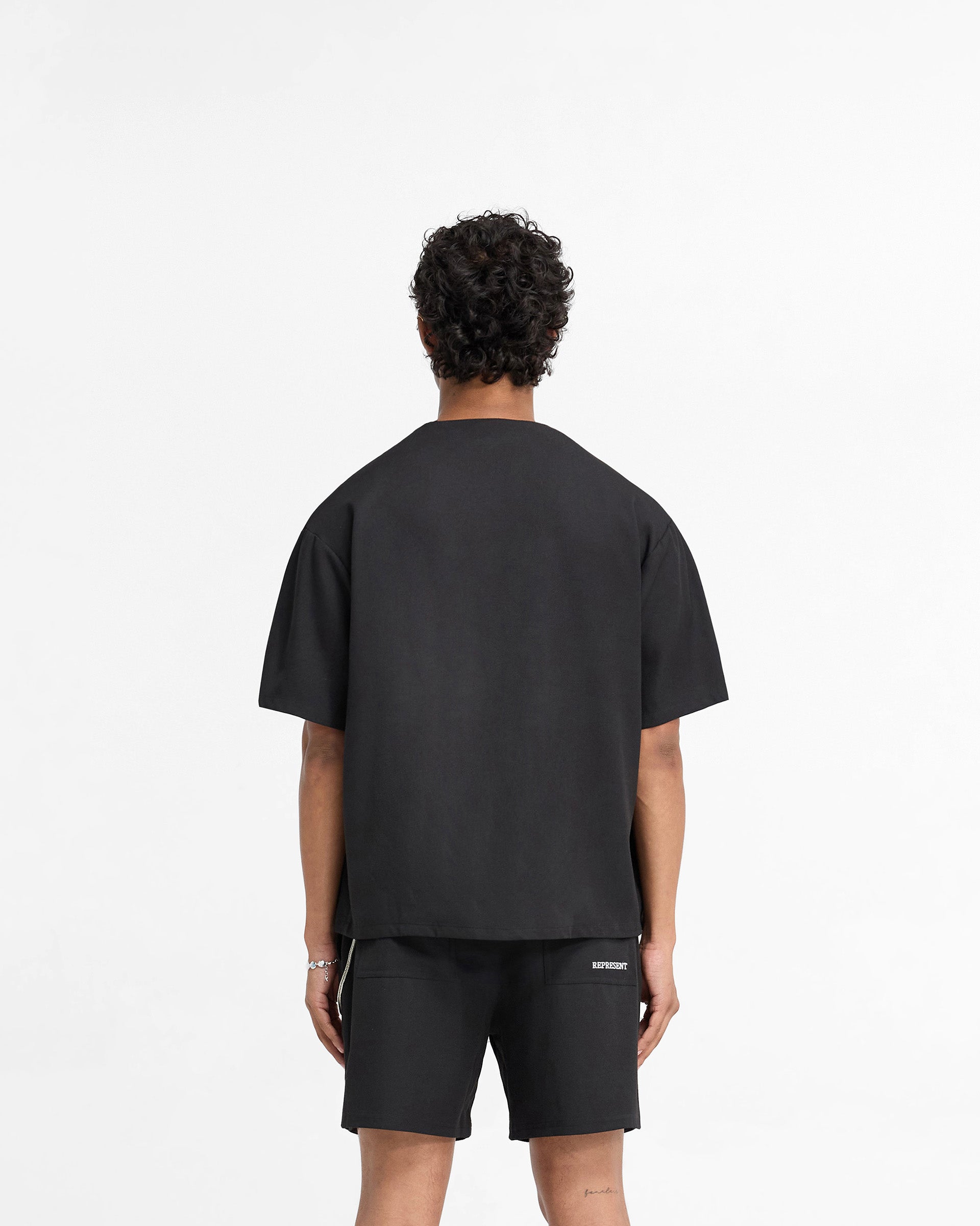 Man wearing a black baseball shirt on a plain white background | Baseball Shirt in Black | Collarless shirt with popper buttons and contrast logo | FW24 Shirts | Represent Clo