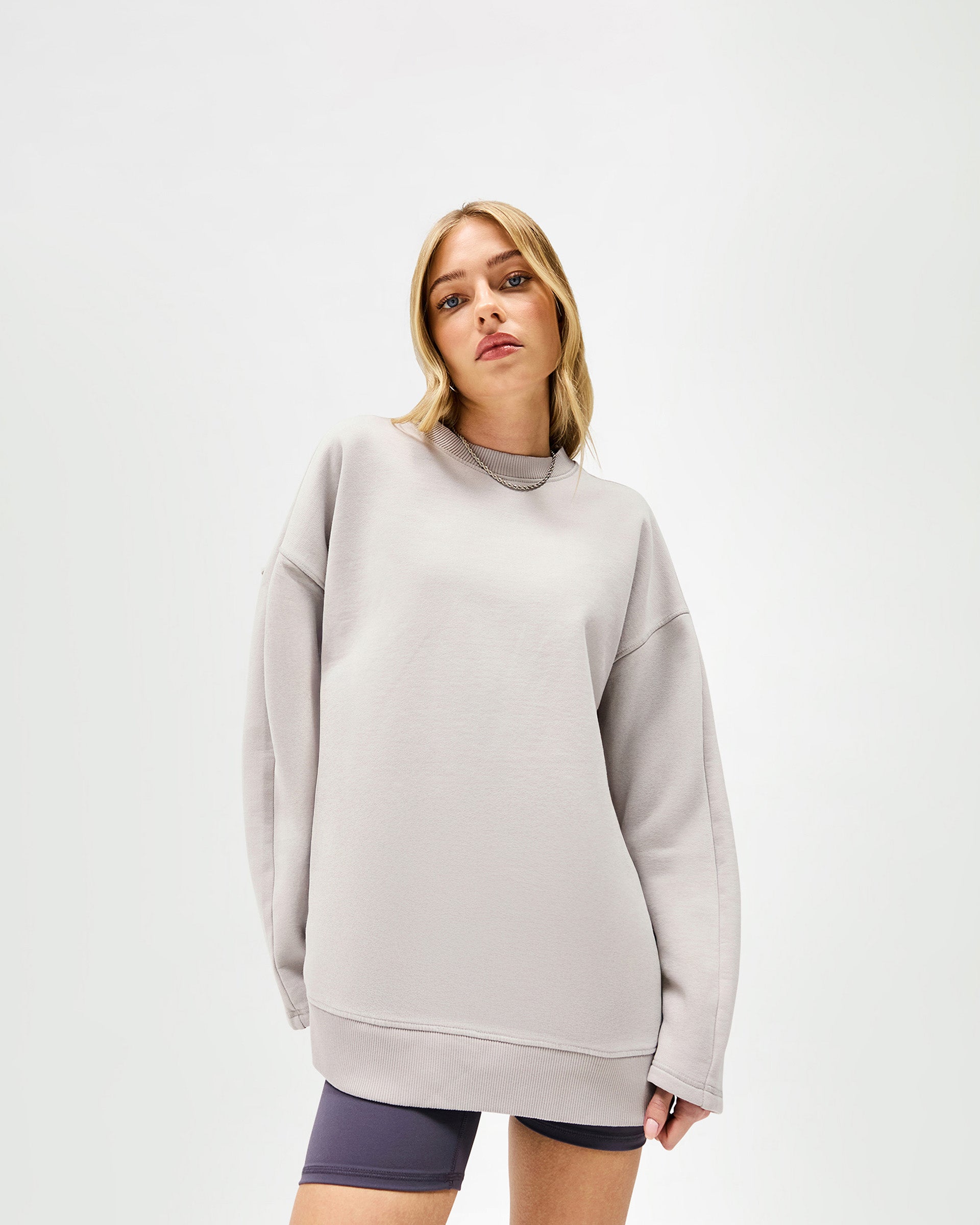 Woman wearing an oversized light grey sweater on a plain white background | Epic Raglan Sweater in Light Grey | Oversized fit raglan sweater with raw edge applique branding | Womens SS25 Sweaters | Represent Clo