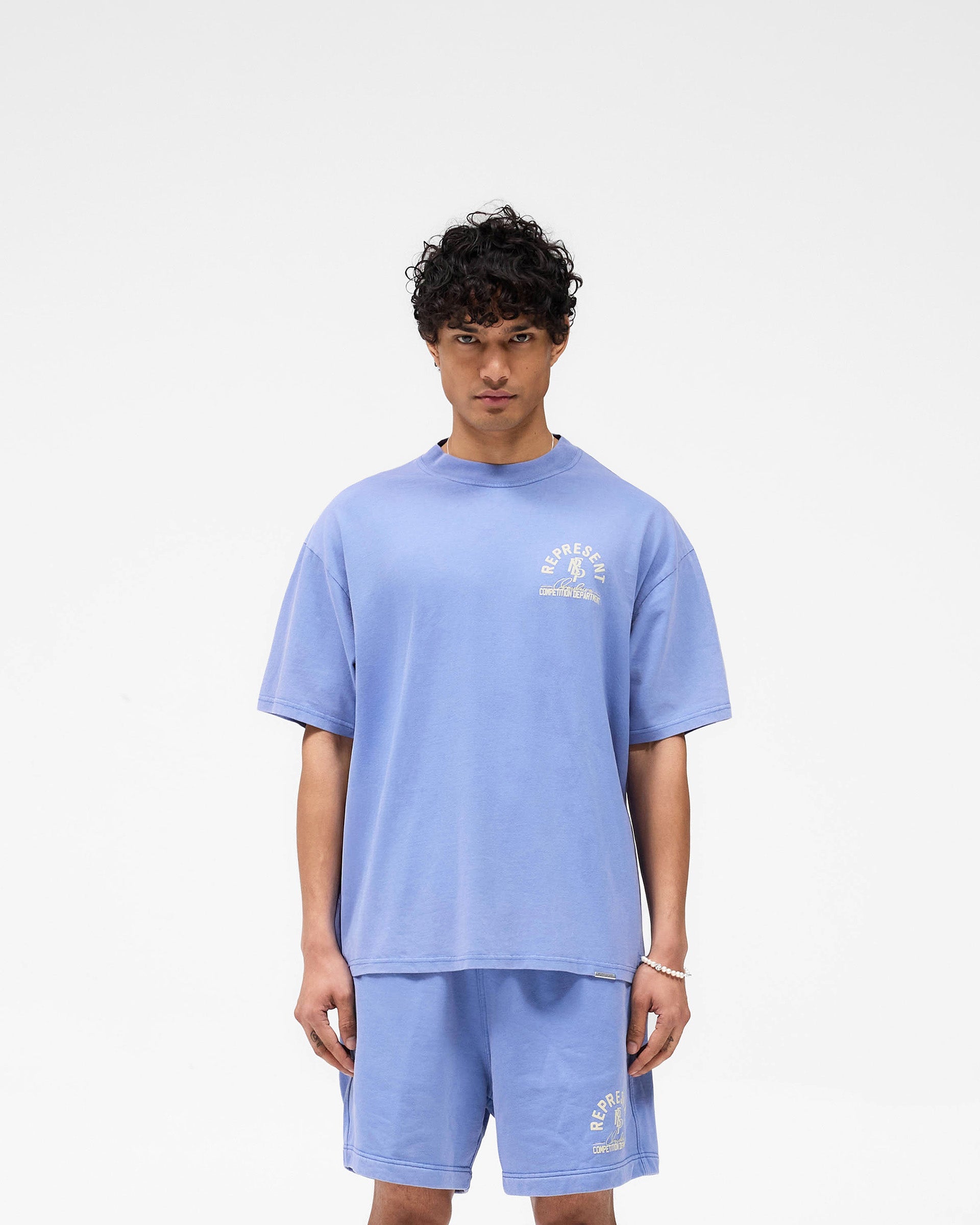 Man wearing a bright blue t-shirt on a plain white background | Competition Department T-Shirt in Bright Blue | Oversized t-shirt with ribbed neckline and chest graphic | SS25 T-Shirts | Represent Clo