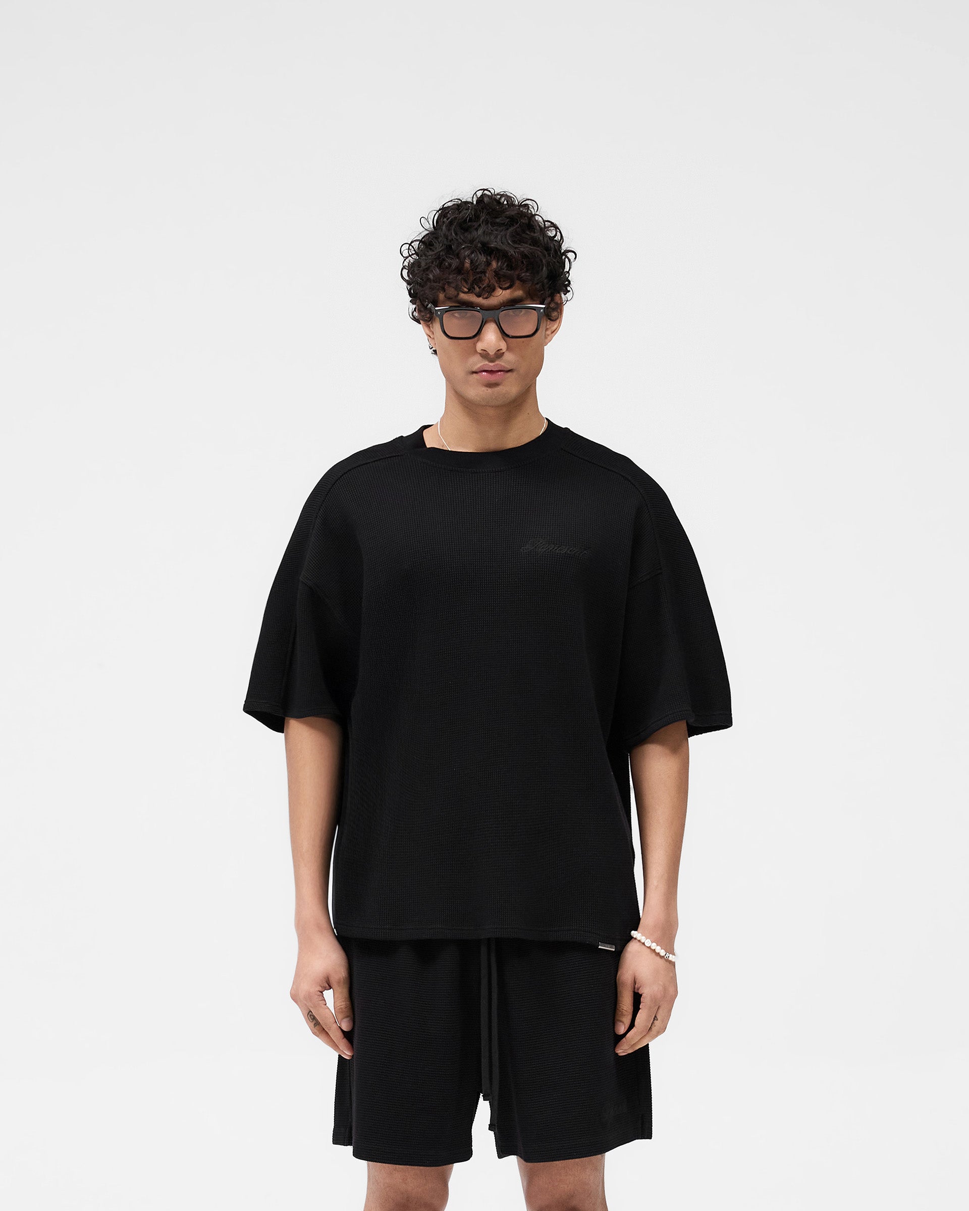 Man wearing a black t-shirt on a plain white background | Waffle T-Shirt in Jet Black | Boxy fit t-shirt crafted from interlock waffle fabric | SS25 T-Shirts | Represent Clo