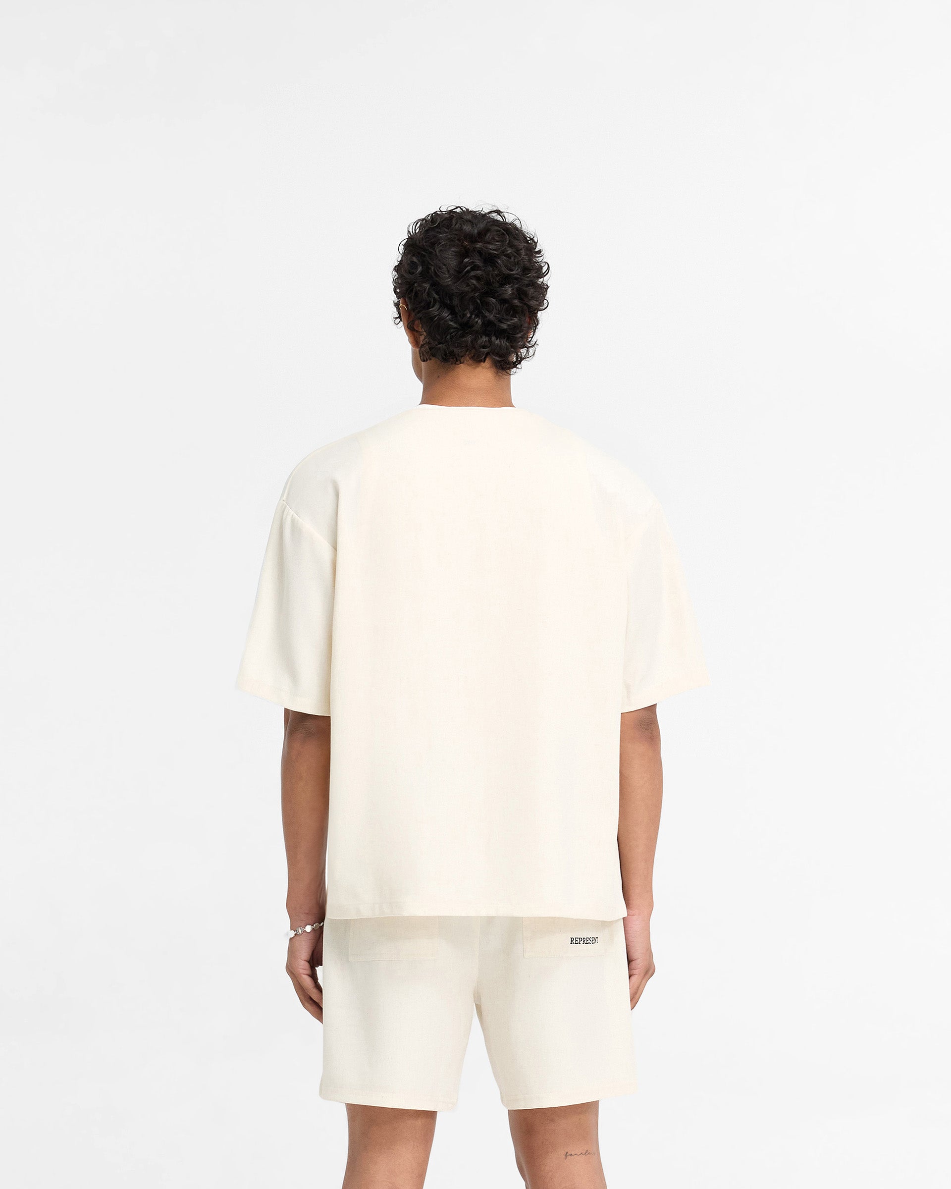 Man wearing an antique white shirt on a plain white background | Baseball Shirt in Antique White | Collarless baseball shirt with embroidered logo | FW24 Shirts | Represent Clo