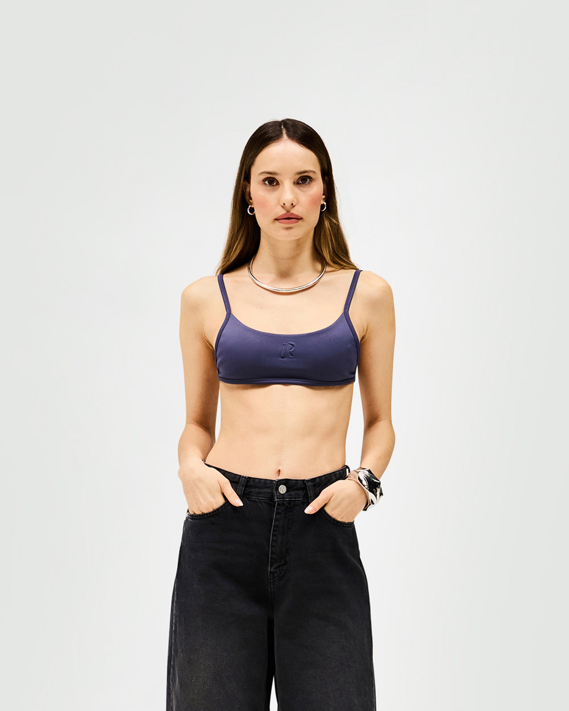 Woman wearing a grey bralette on a plain white background | Control Bralette in Graphite | Neoprene bralette with adjustable fit and embossed Initial R | Womens SS25 Tops | Represent Clo