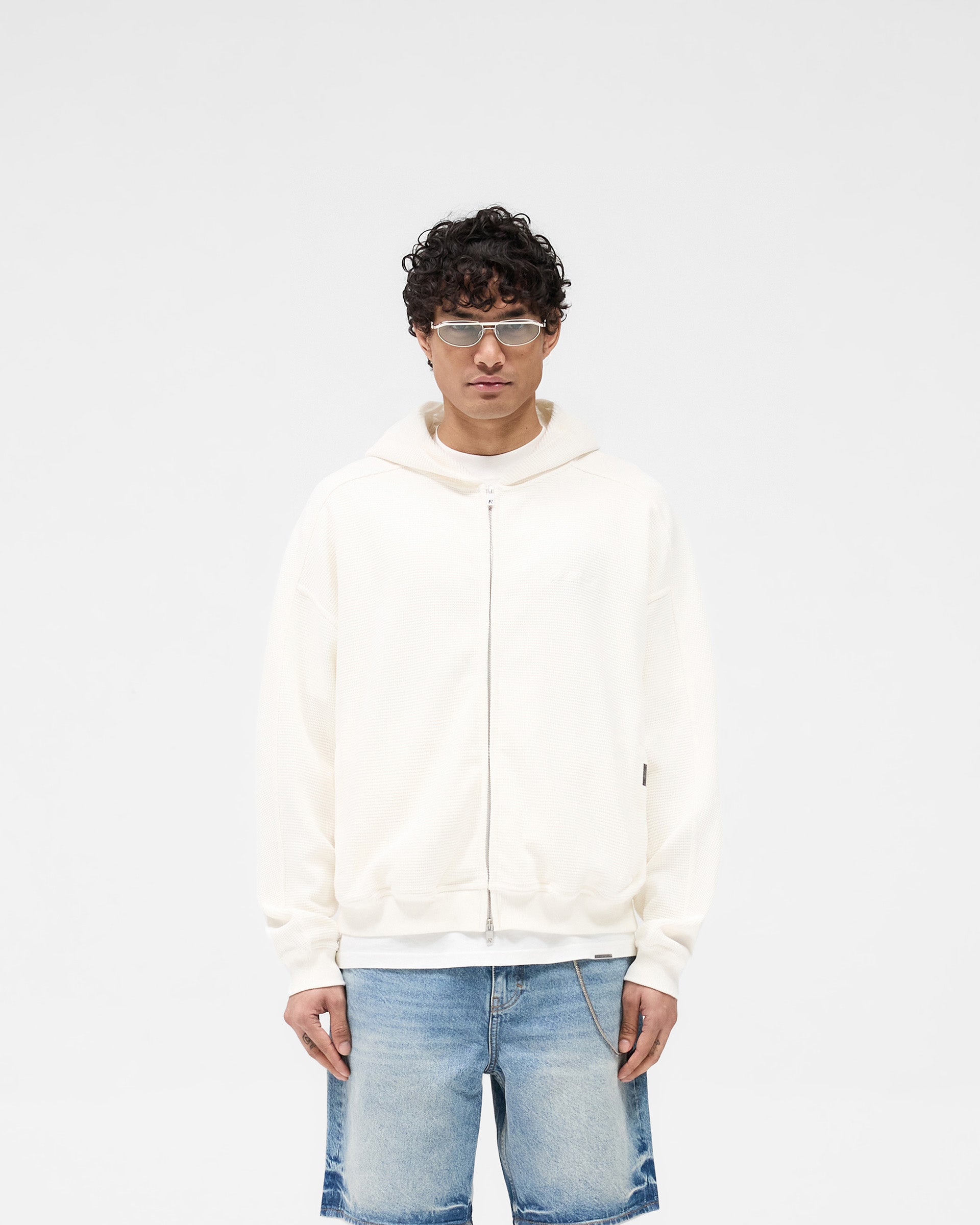 Man wearing an oversized white hoodie on a plain white background | Waffle Zip Through Hoodie in Flat White | Boxy fit hoodie with branded zipper and logo | SS25 Hoodies | Represent Clo
