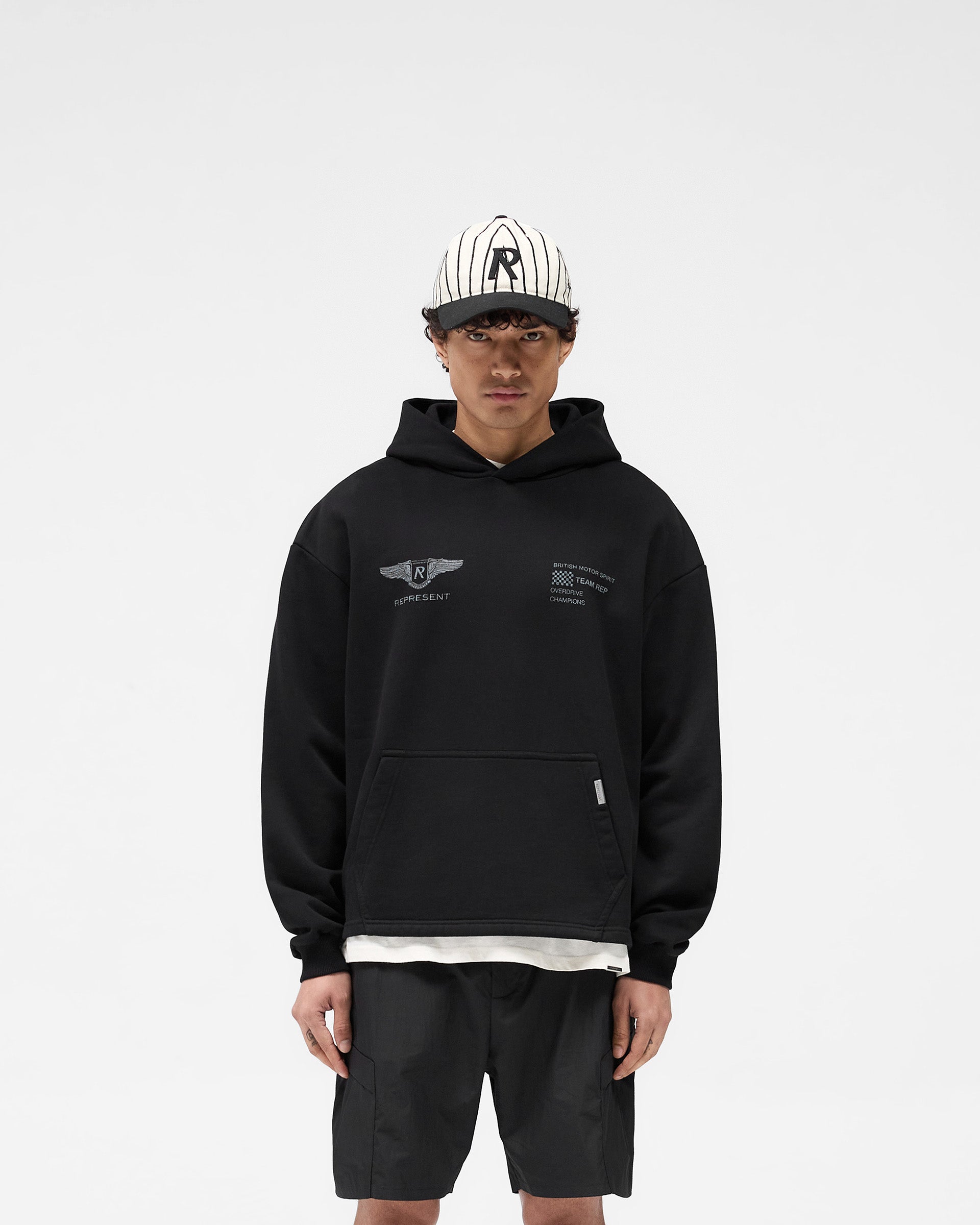 Man wearing an oversized black hoodie on a plain white background | Team Rep Hoodie in Black | Vintage worn graphic oversized hoodie | SS25 Hoodies | Represent Clo