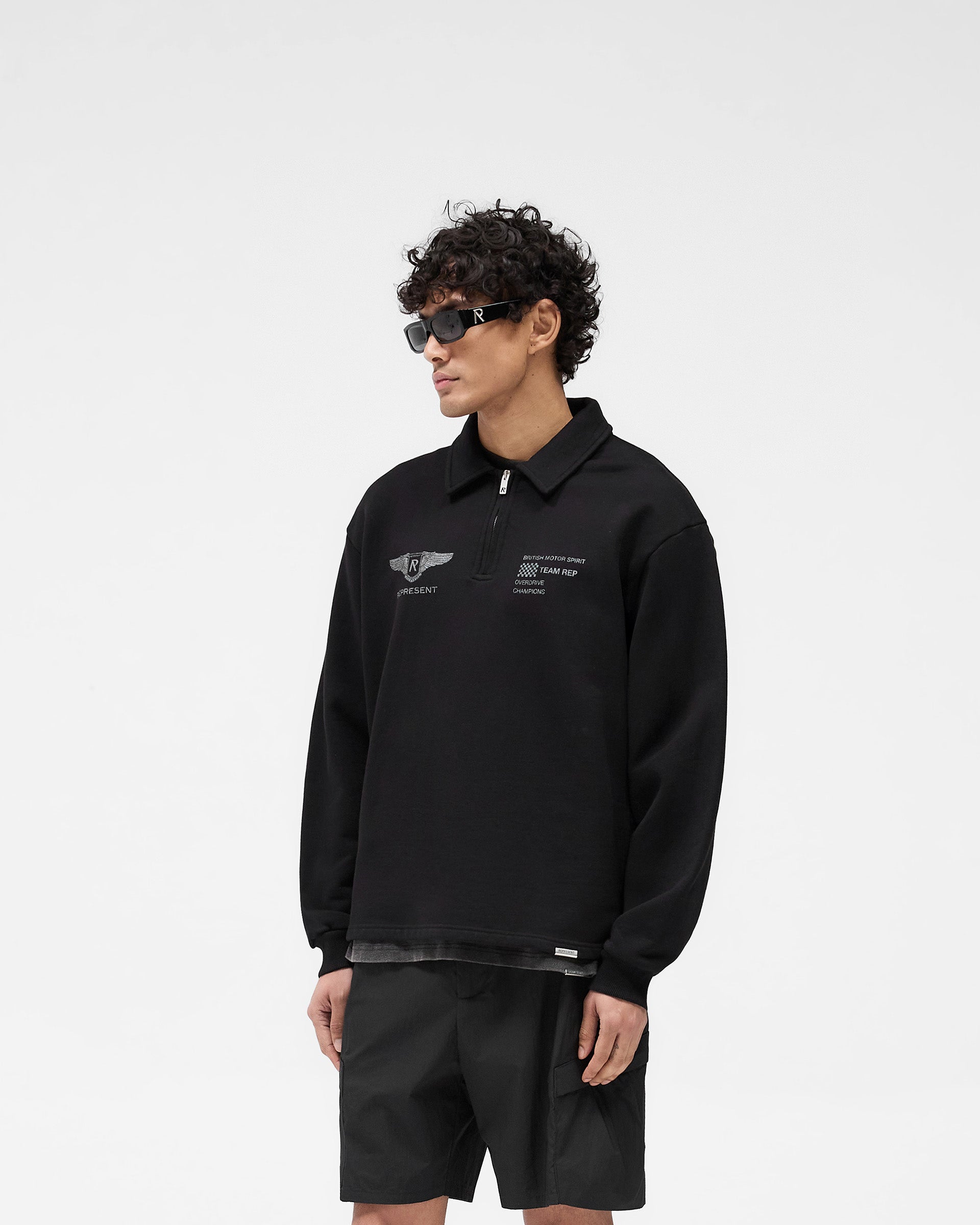 Man wearing a black quarter zip sweater on a plain white background | Team Rep Quarter Zip in Jet Black | Oversized sweater with vintage graphics | SS25 Sweaters | Represent Clo